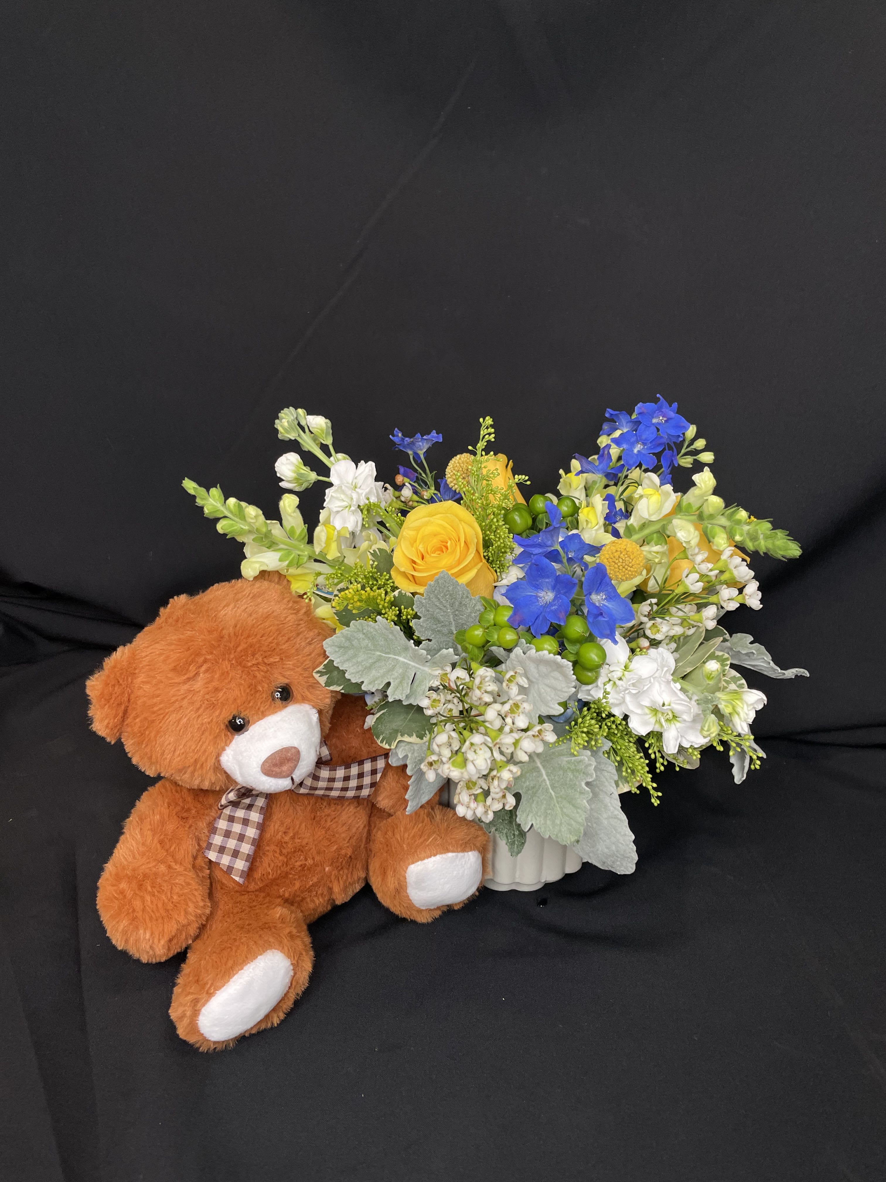 Bouquet of yellow, blue, and white flowers beside a teddy bear