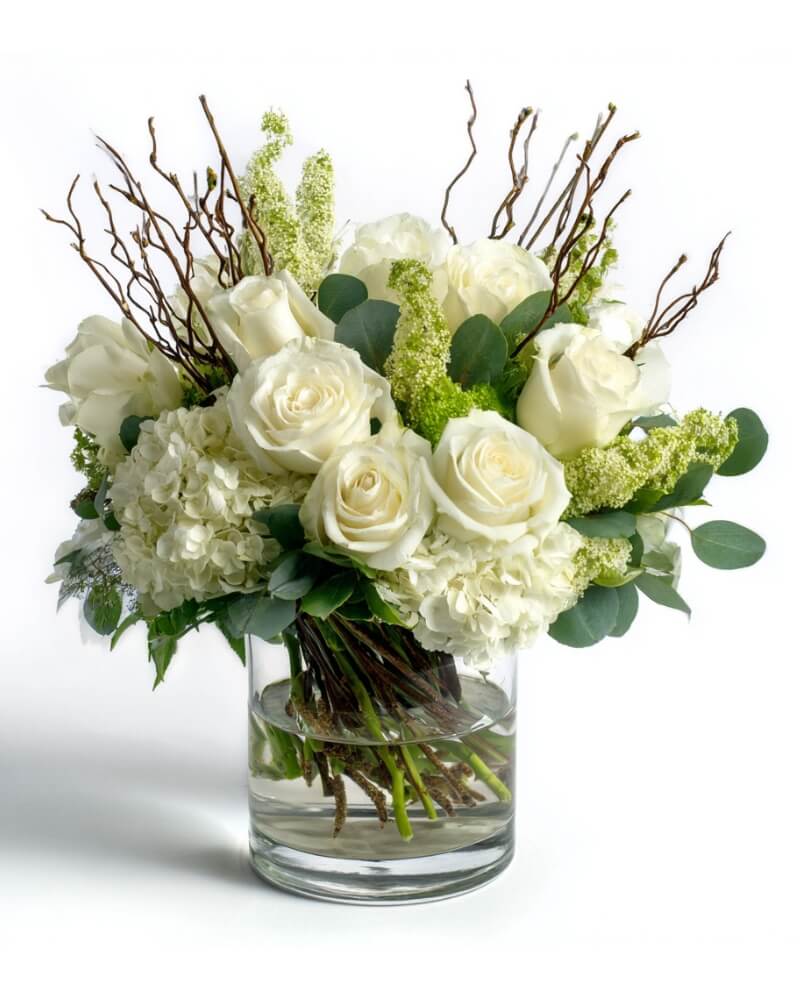 White roses and hydrangeas in a glass vase with branches