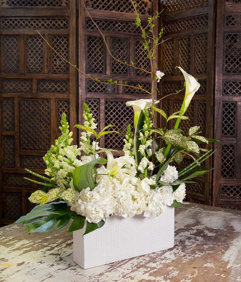 White floral arrangement with calla lilies and hydrangeas in a white rectangular vase