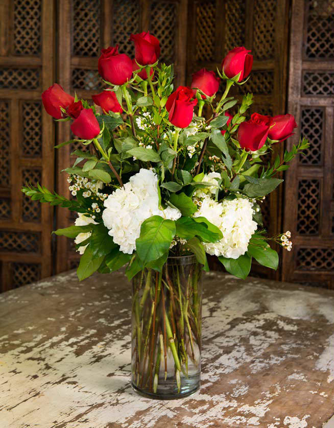 Red roses and white hydrangeas arranged in a clear glass vase.