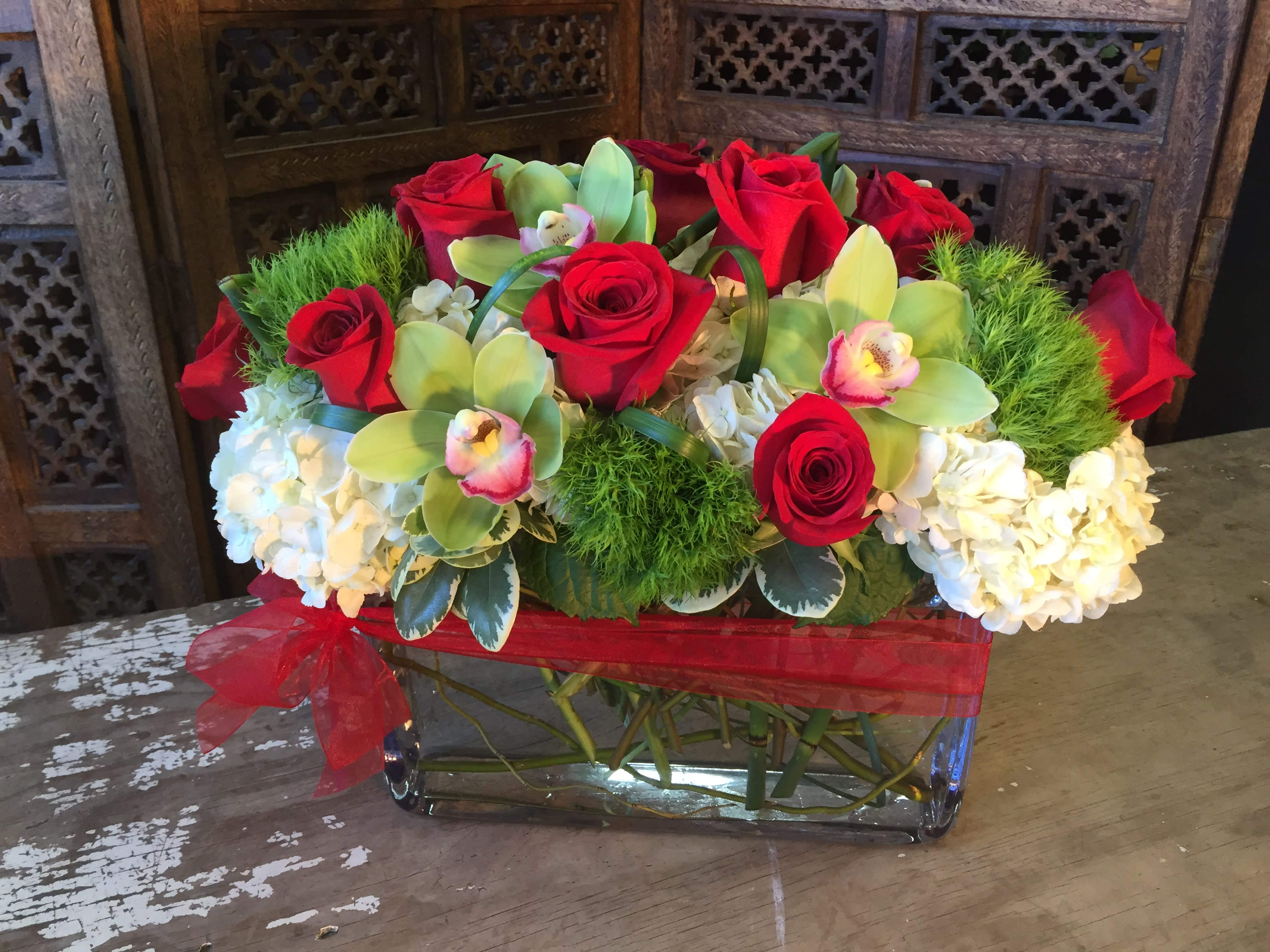 Red roses and white hydrangeas in a glass vase with a red ribbon