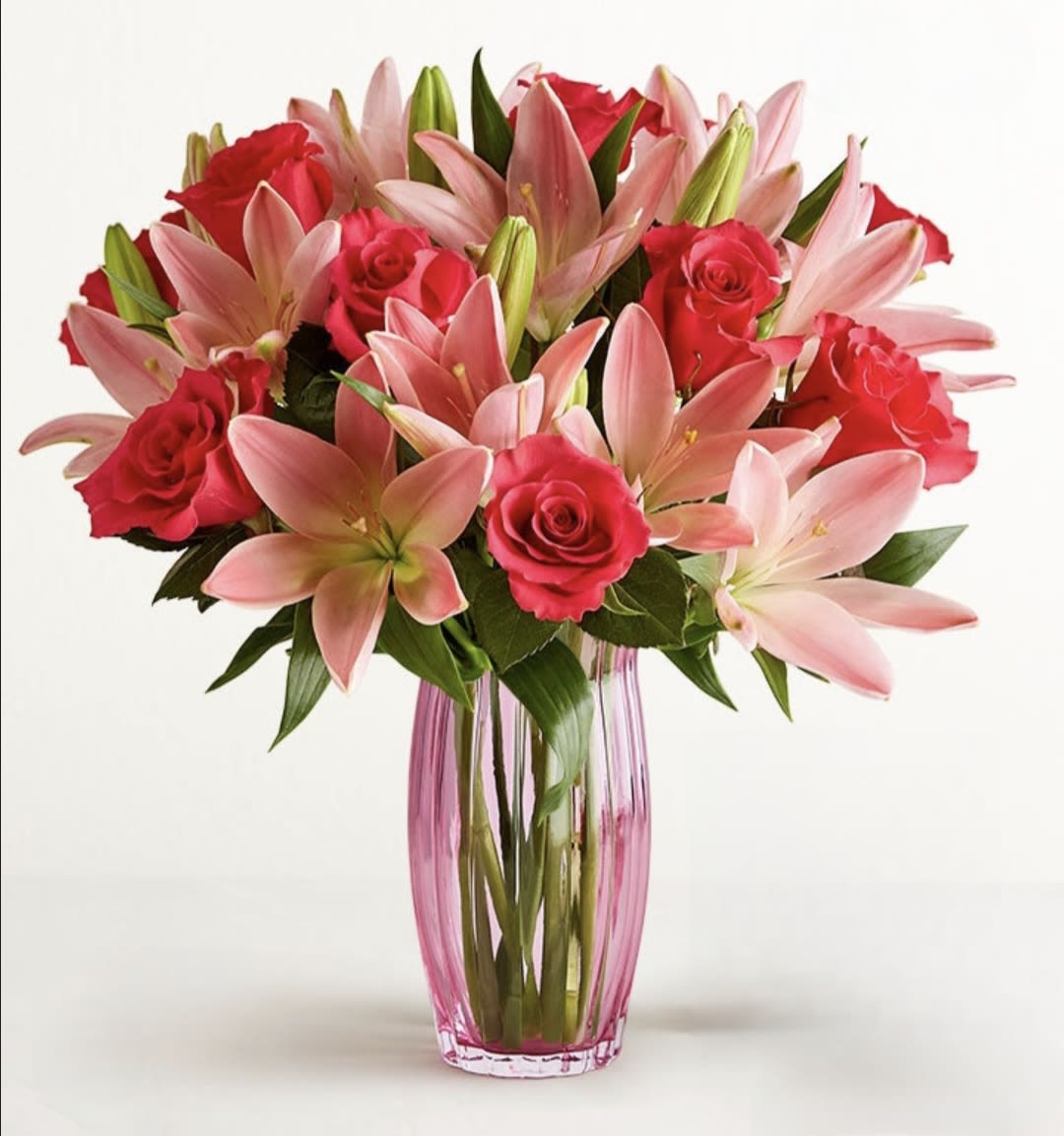 Pink lilies and red roses arranged in a tall glass vase