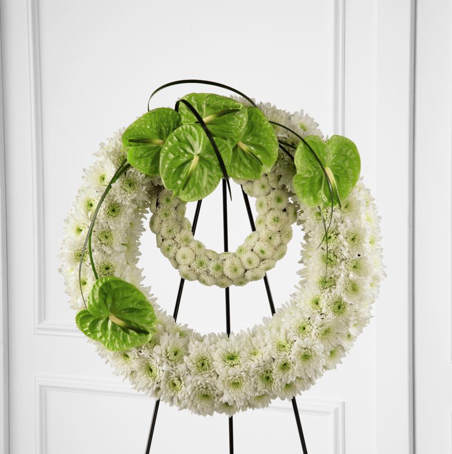 White floral wreath on a black stand with bright green anthurium accents