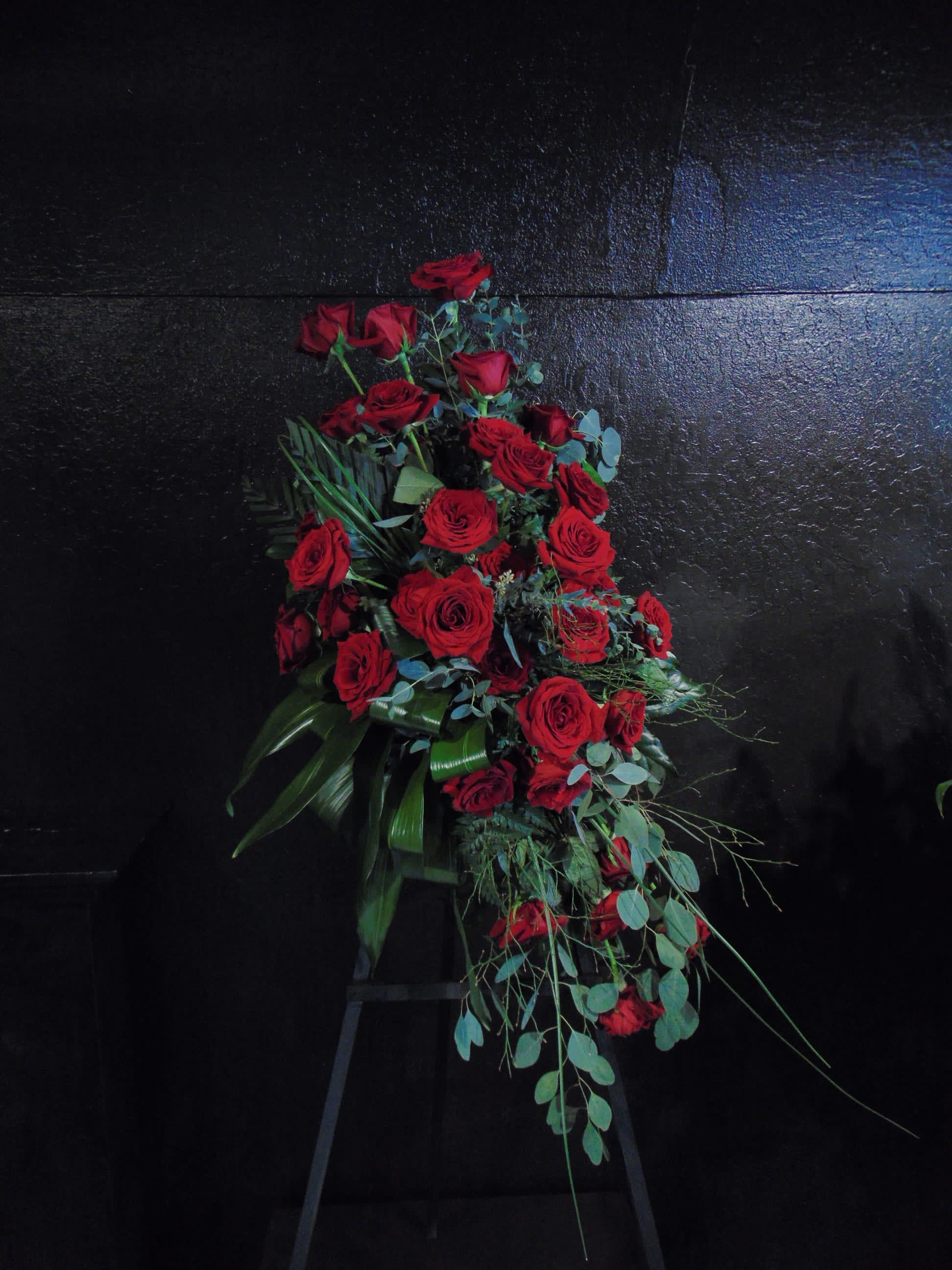 Tall standing spray of red roses arranged in a cascading shape on a black stand.