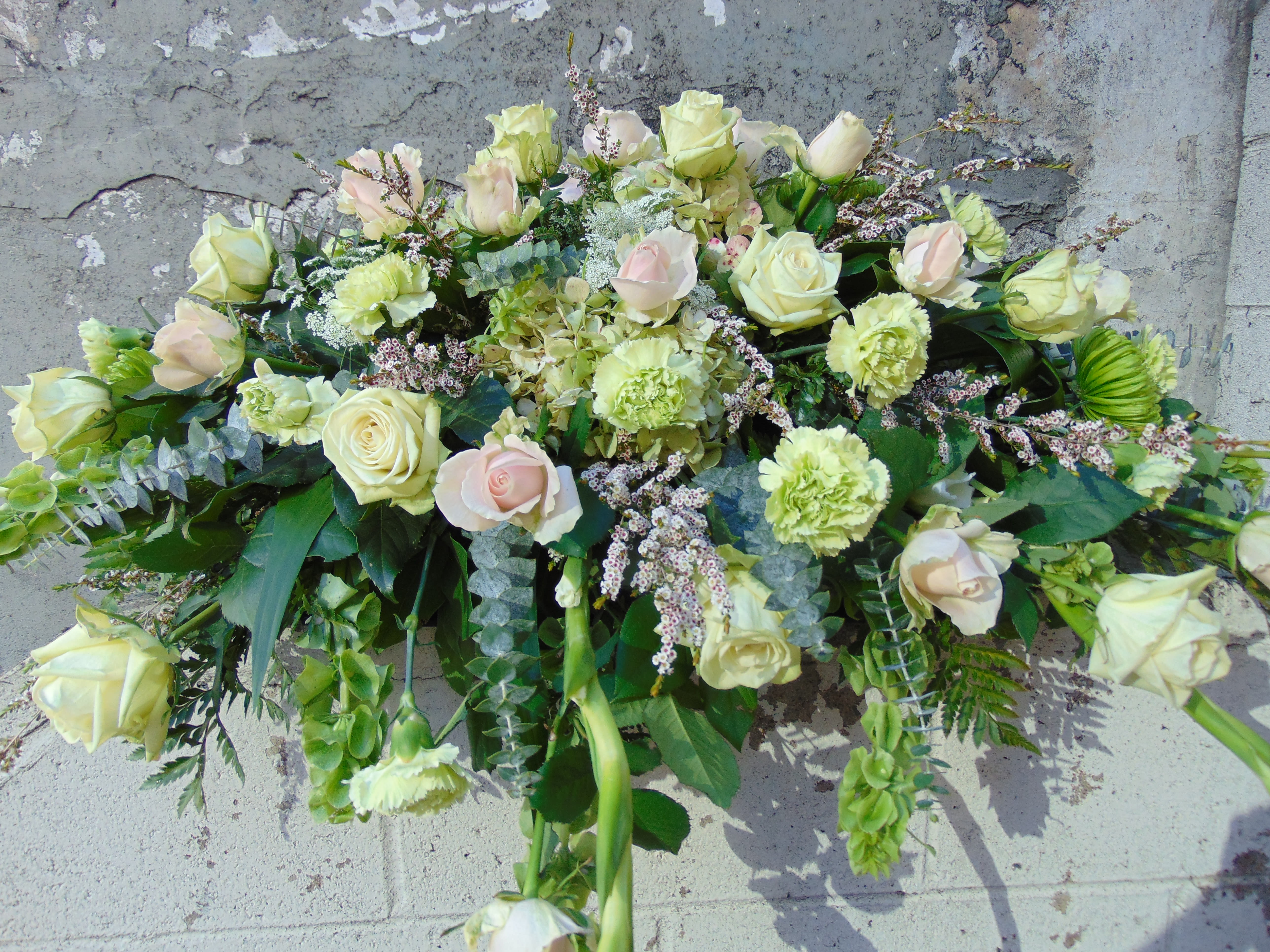 Long arrangement of cream roses and green carnations in a soft, cascading design