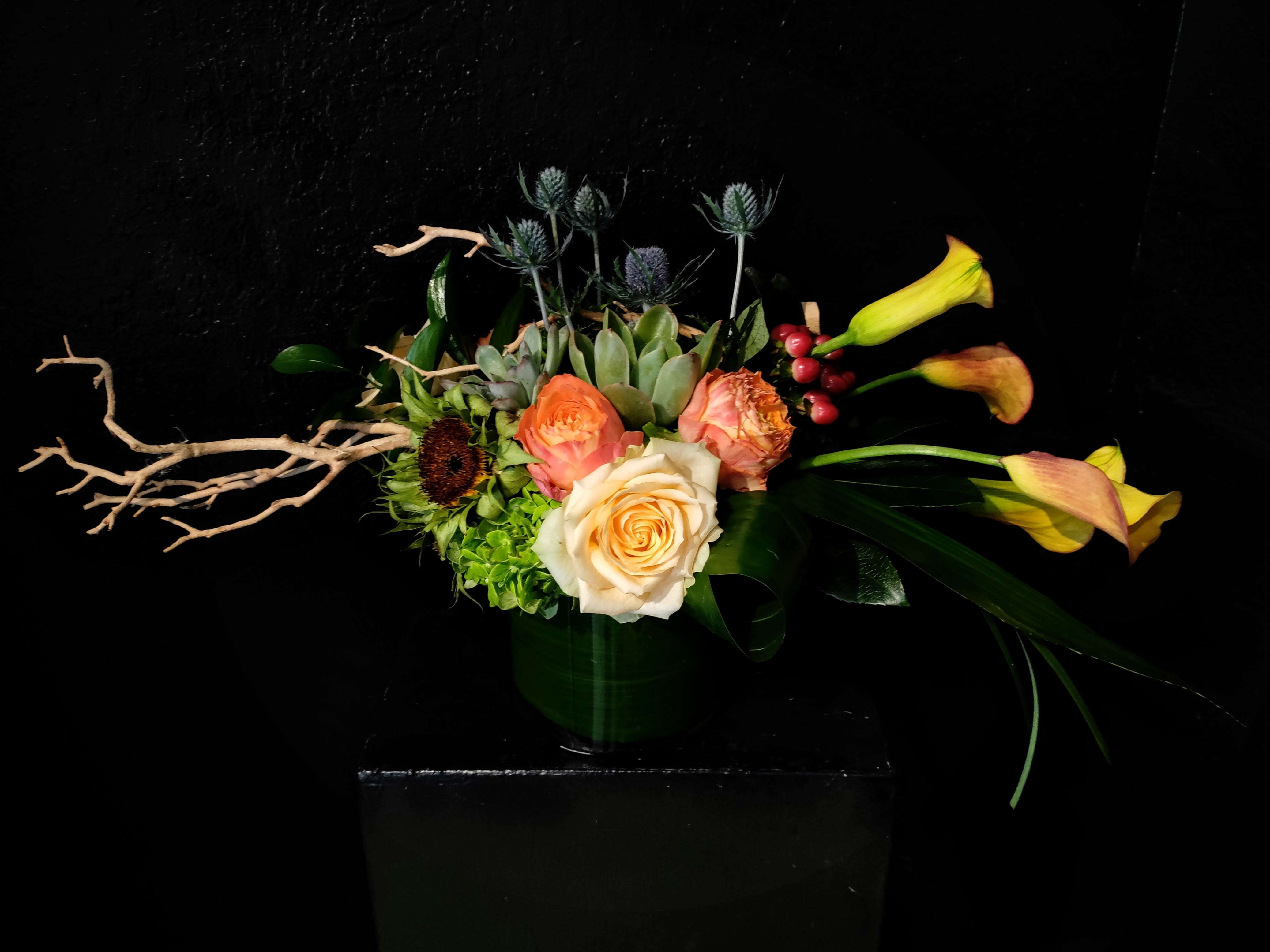 Arrangement of peach roses and yellow calla lilies in a dark vase