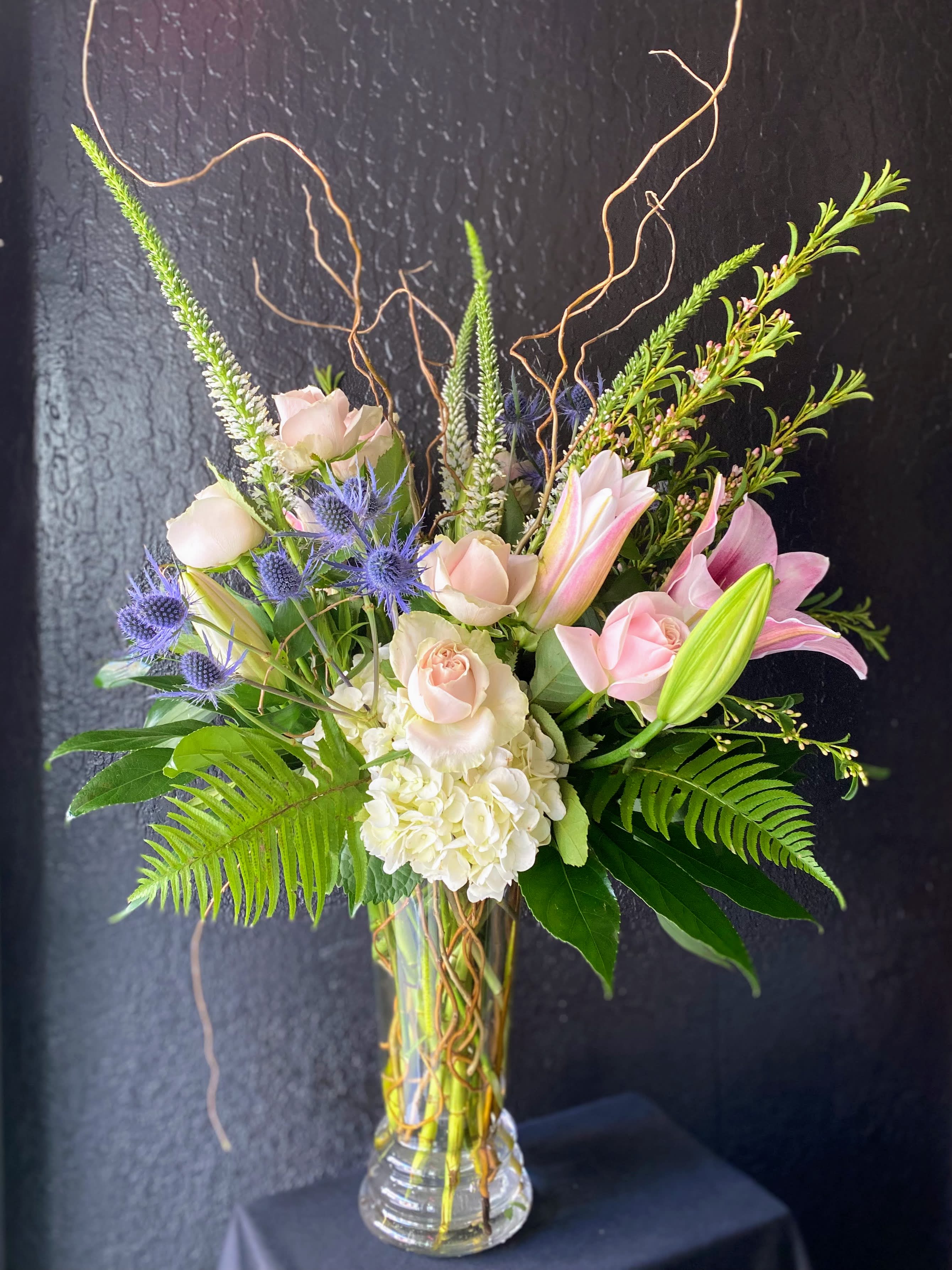 Tina  - A fragrant arrangement with pink roses, lilles, and blues in a cluster-style design that celebrates femininity. The container measures roughly 12" tall  