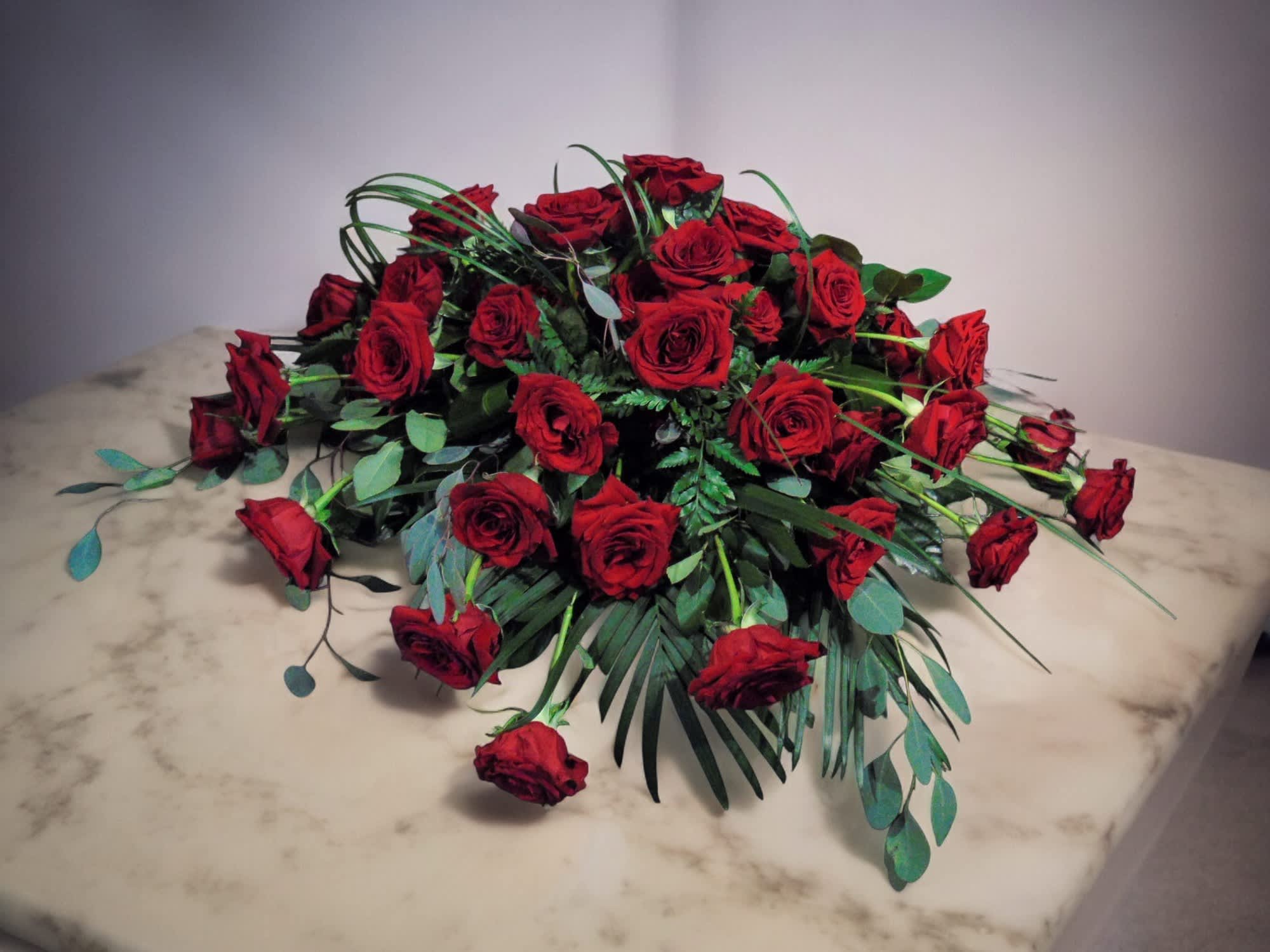 Low, elongated arrangement of red roses spread across a marble surface