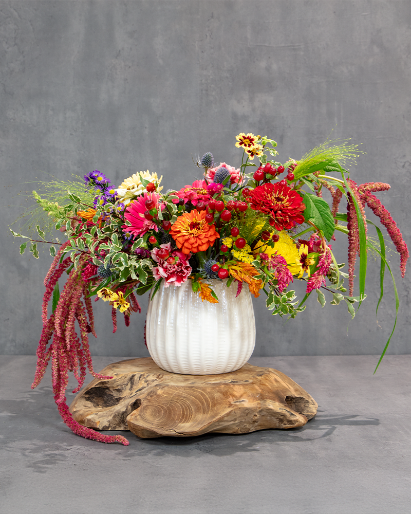 Colorful mixed flower arrangement in a white vase on a wooden base