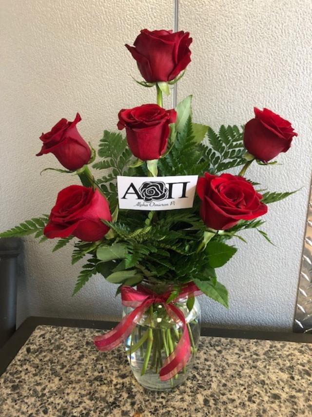 Six red roses arranged in a clear glass vase with a red ribbon