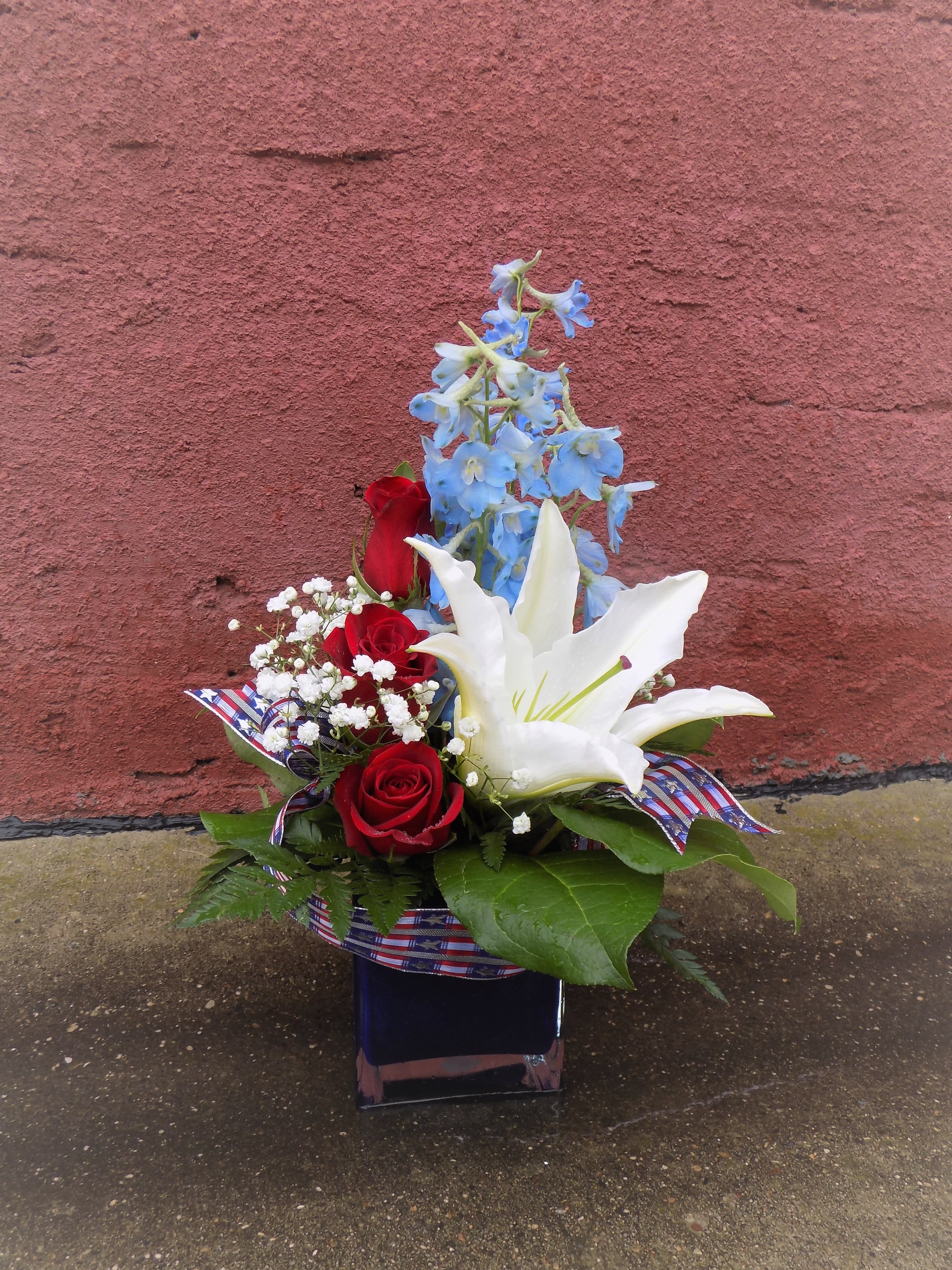 Red roses and a white lily with blue flowers in a square vase