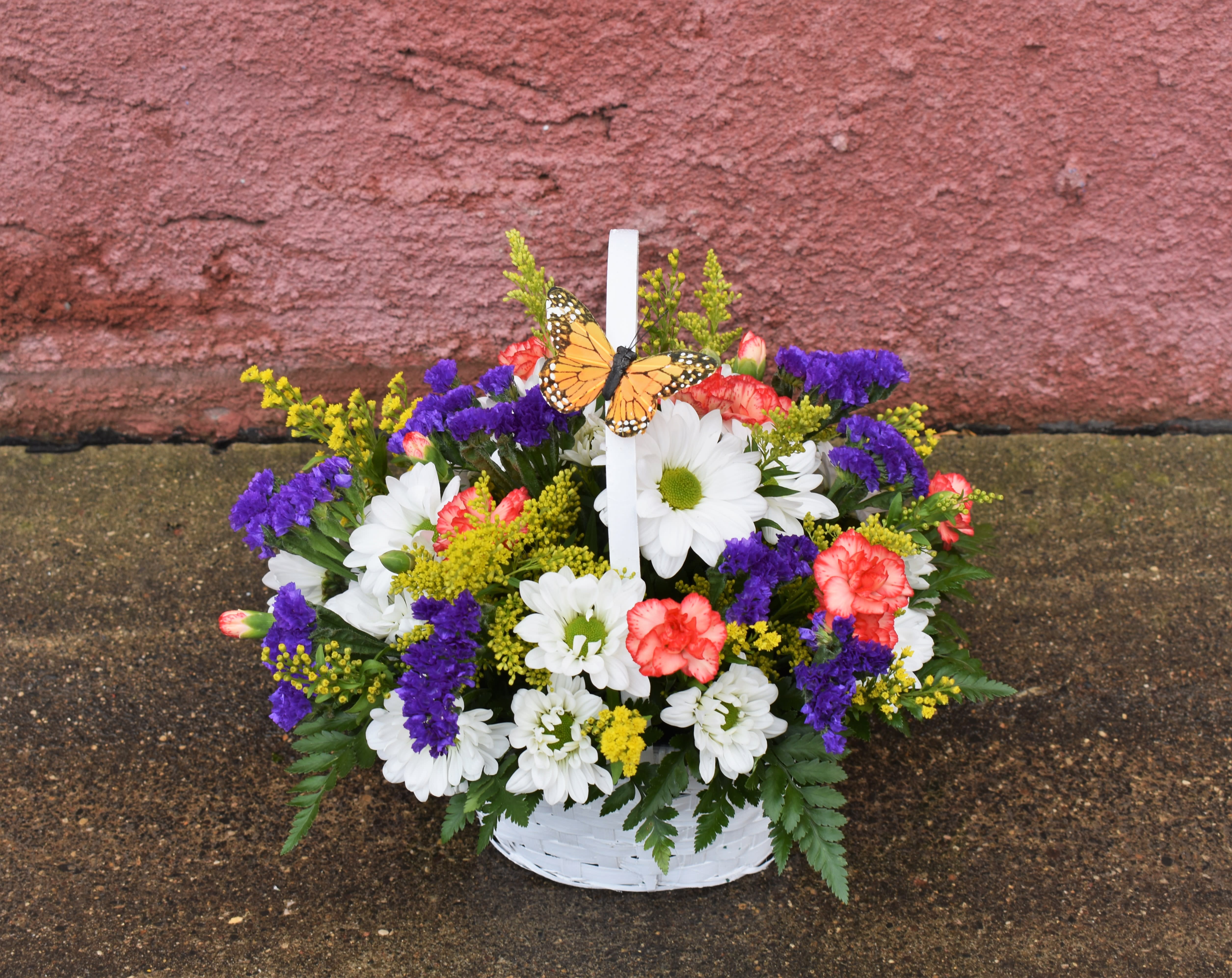Basket of white daisies, purple statice, and pink carnations with a butterfly pick
