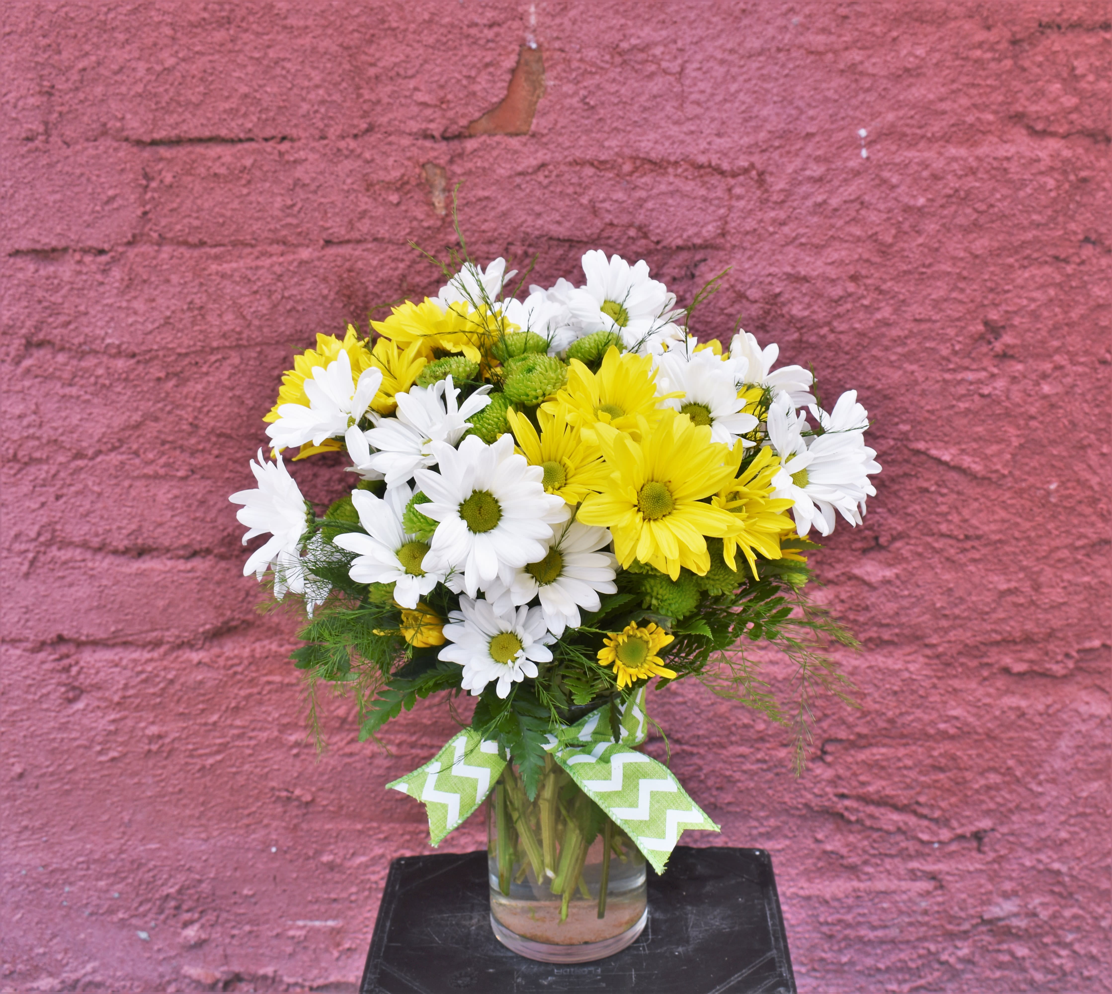 Yellow and white daisy bouquet in a glass vase with a chevron ribbon