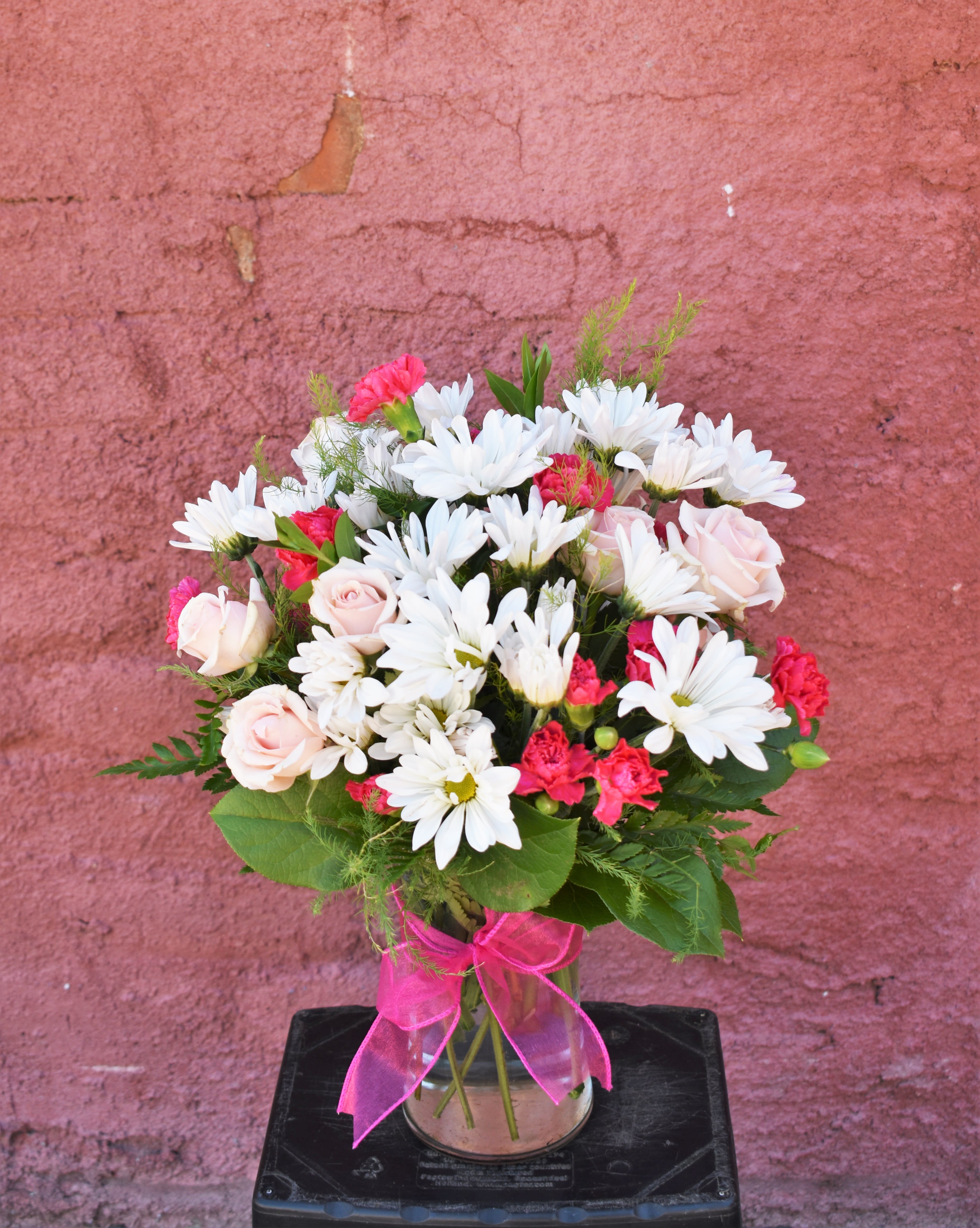 Bouquet of white daisies and pink roses in a glass vase with a pink ribbon