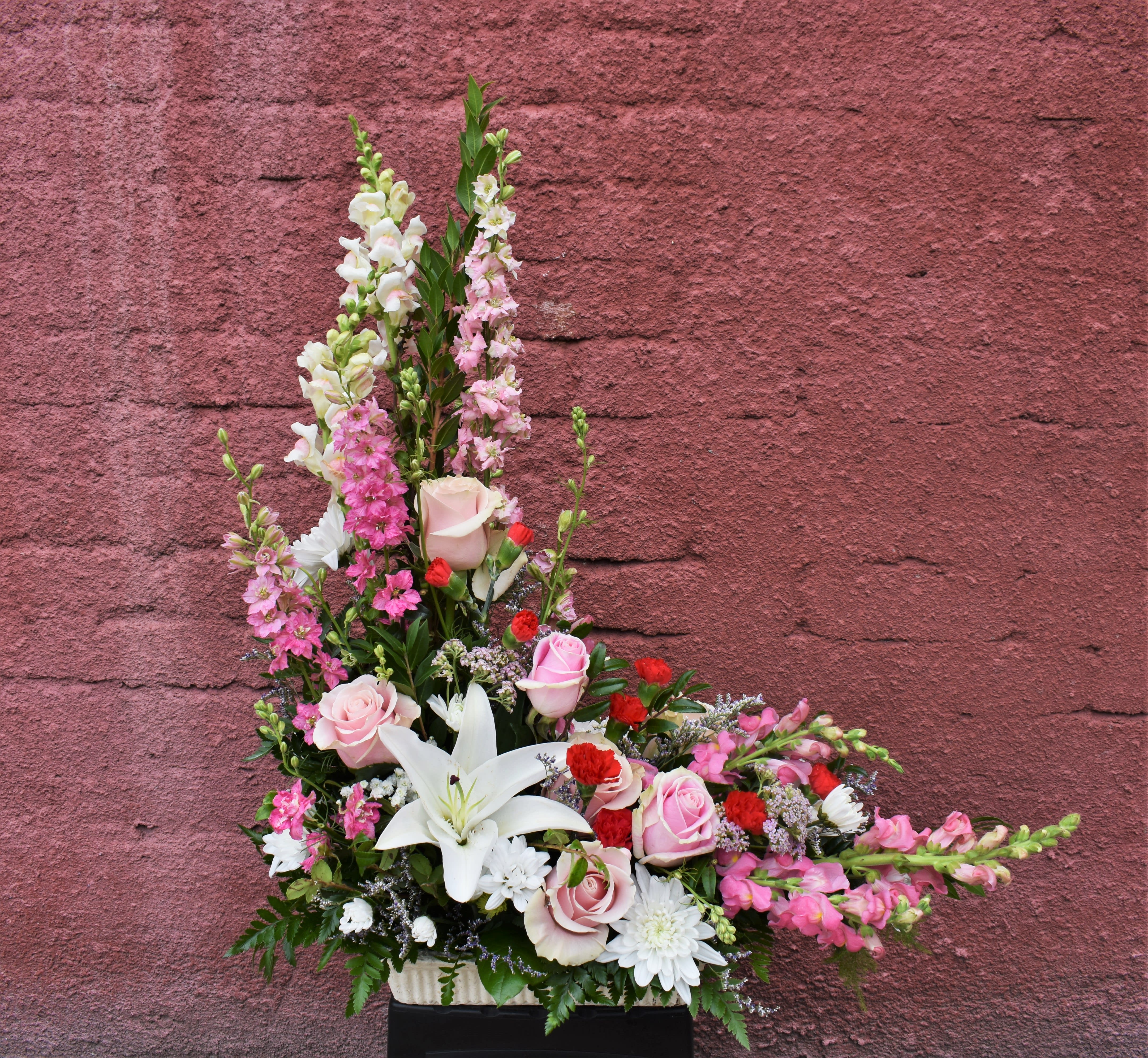 Tall pink and white floral arrangement with roses and lilies in a container