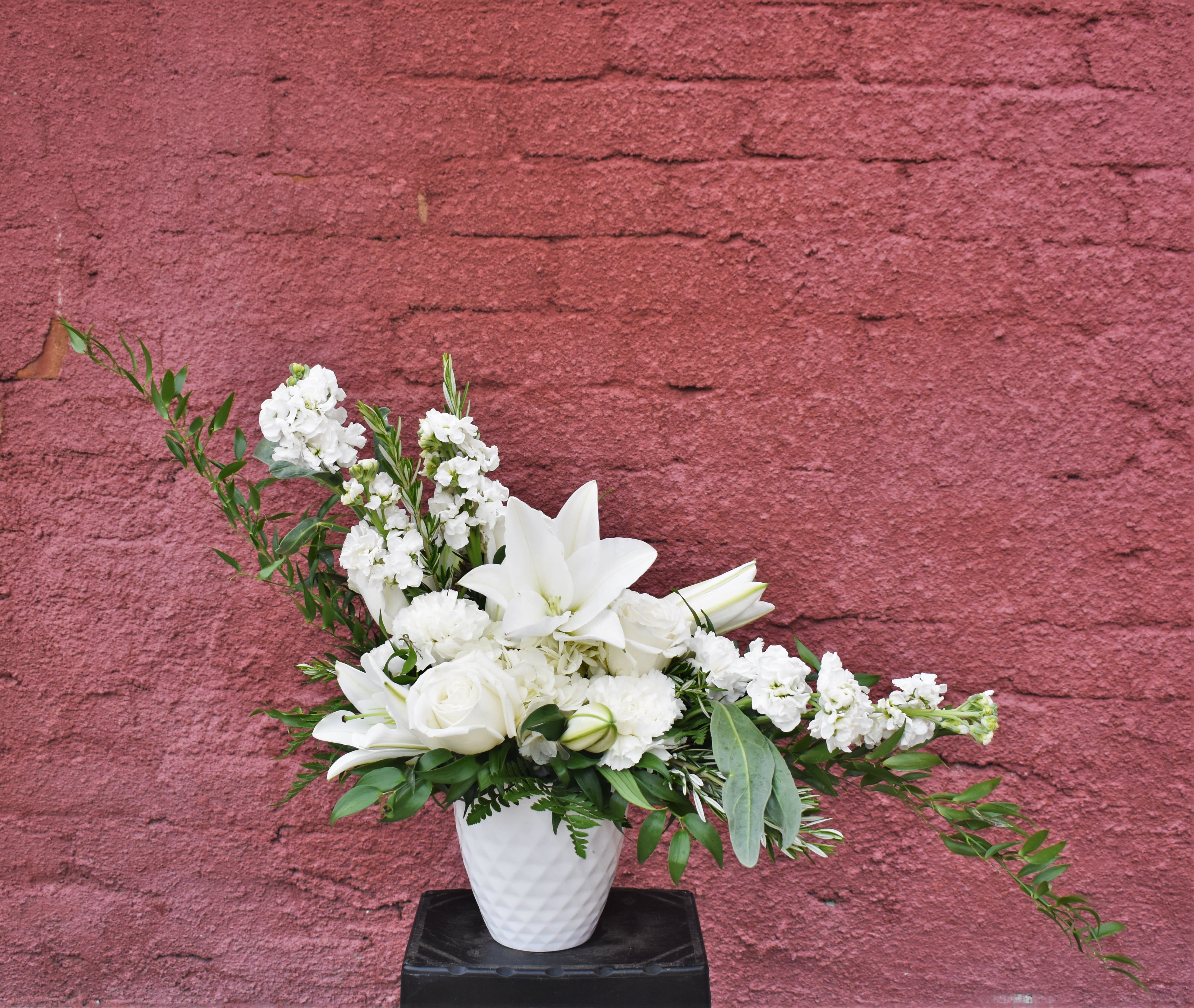 White floral arrangement in a white vase with lilies and roses