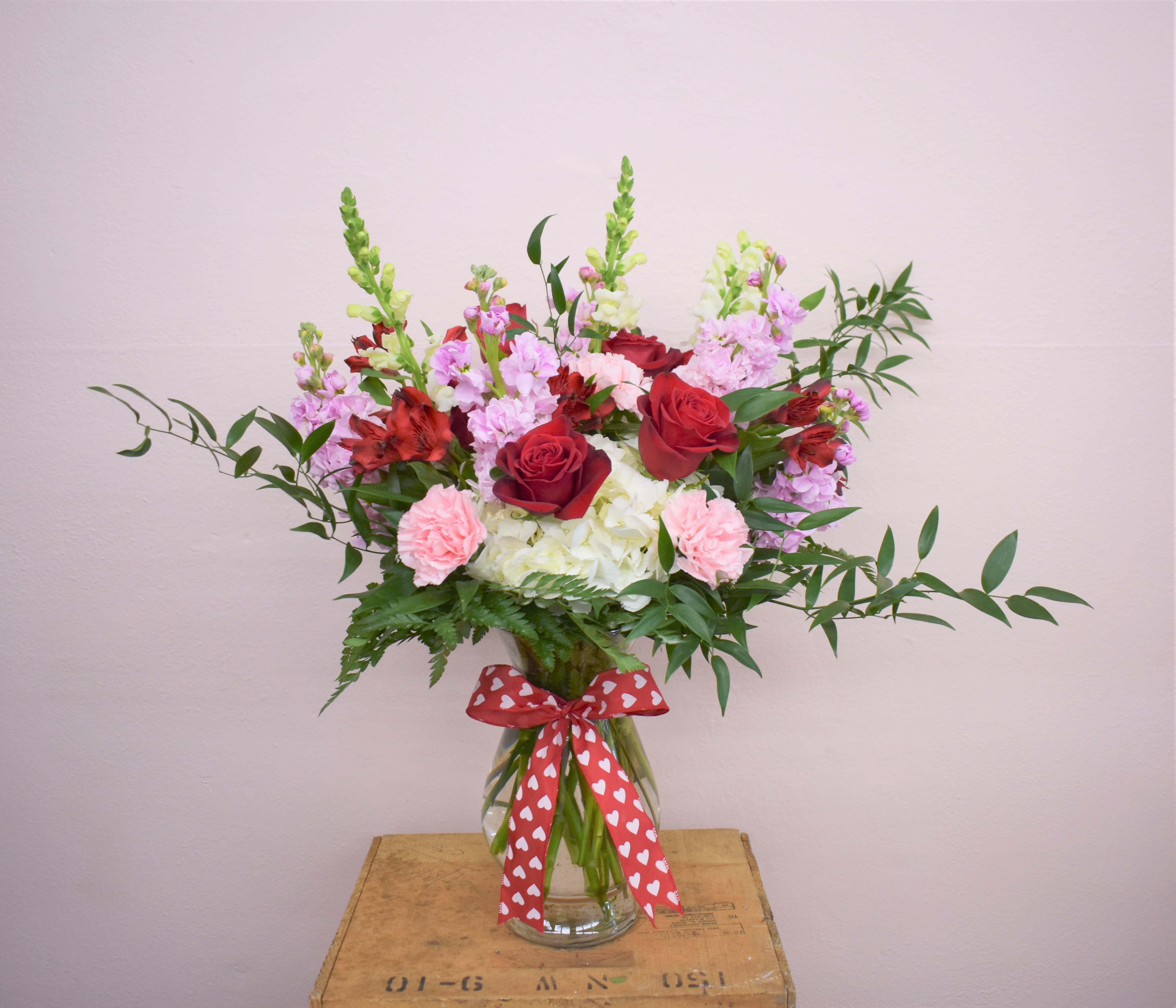 Mixed bouquet of red roses, pink carnations, and white hydrangeas in a glass vase