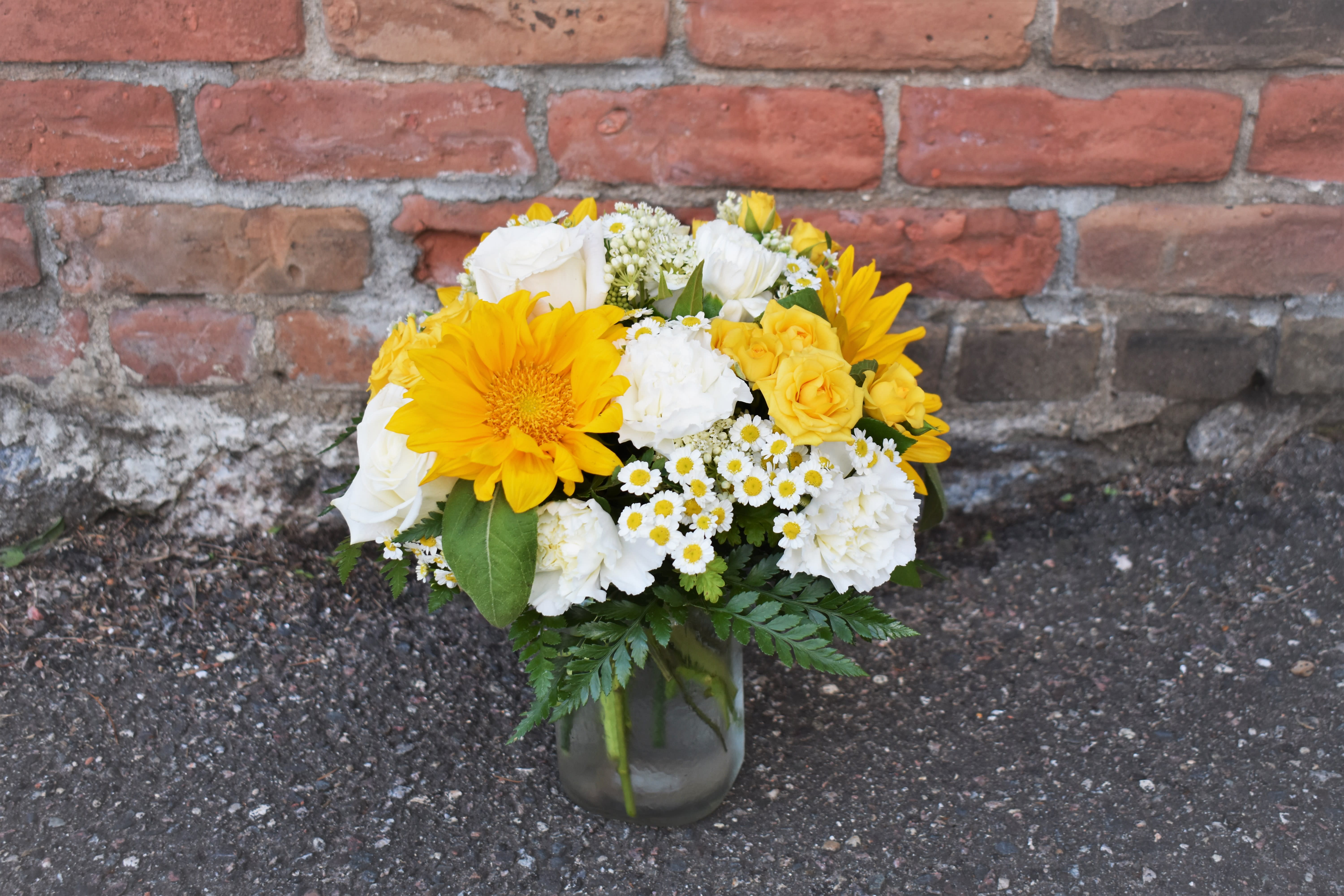 Pocketful of Sunshine - Bright yellow sunflowers, yellow spray roses, chamomile, white roses and carnations, and lush greenery are arranged in a clear vase and perfect to brighten anyone's day!