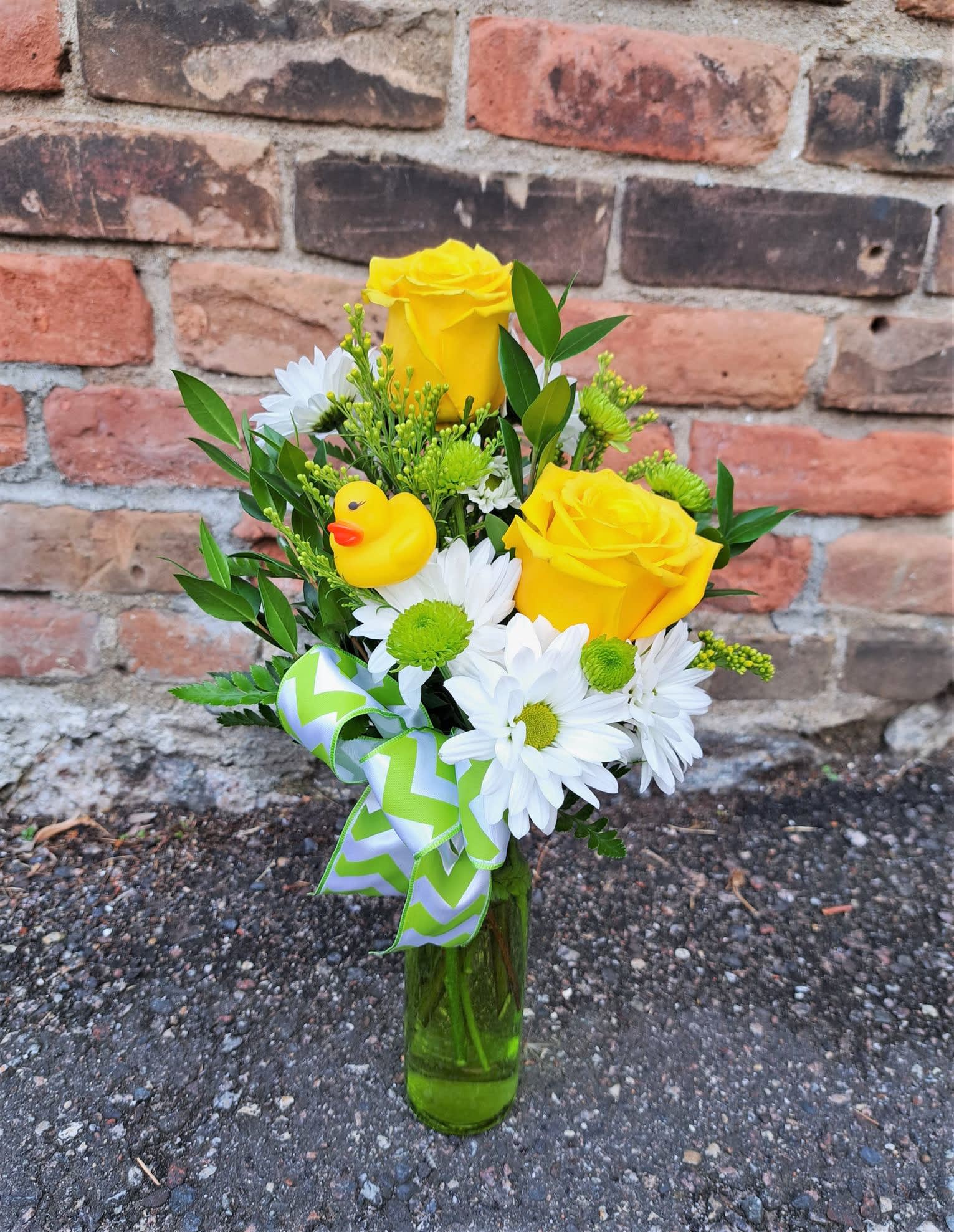 Yellow roses and white daisies in a glass vase with a duck ornament