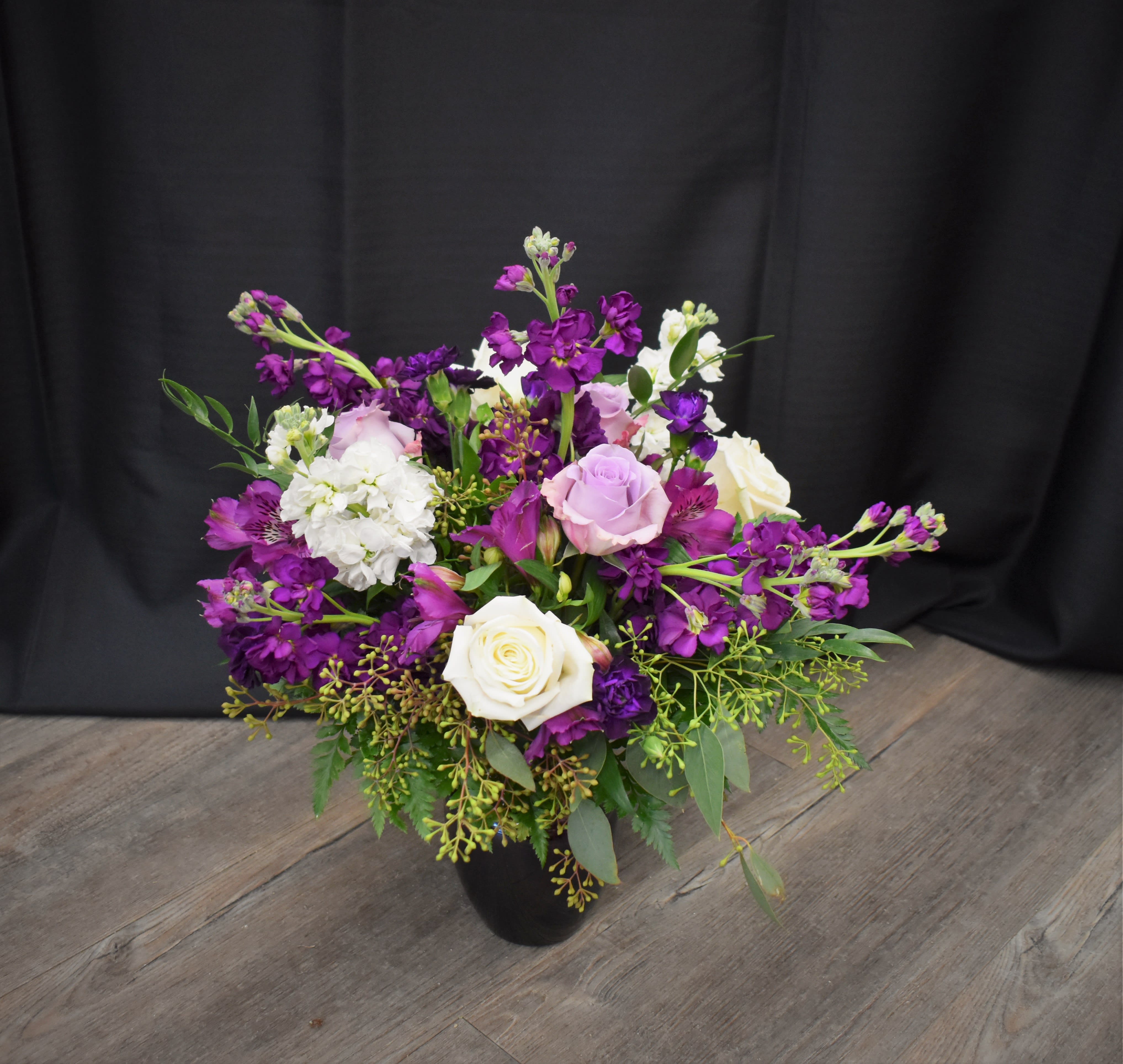 Purple and white mixed flower arrangement in a black vase