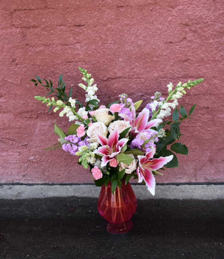 Bouquet of pink lilies, white roses, and purple flowers in a red glass vase