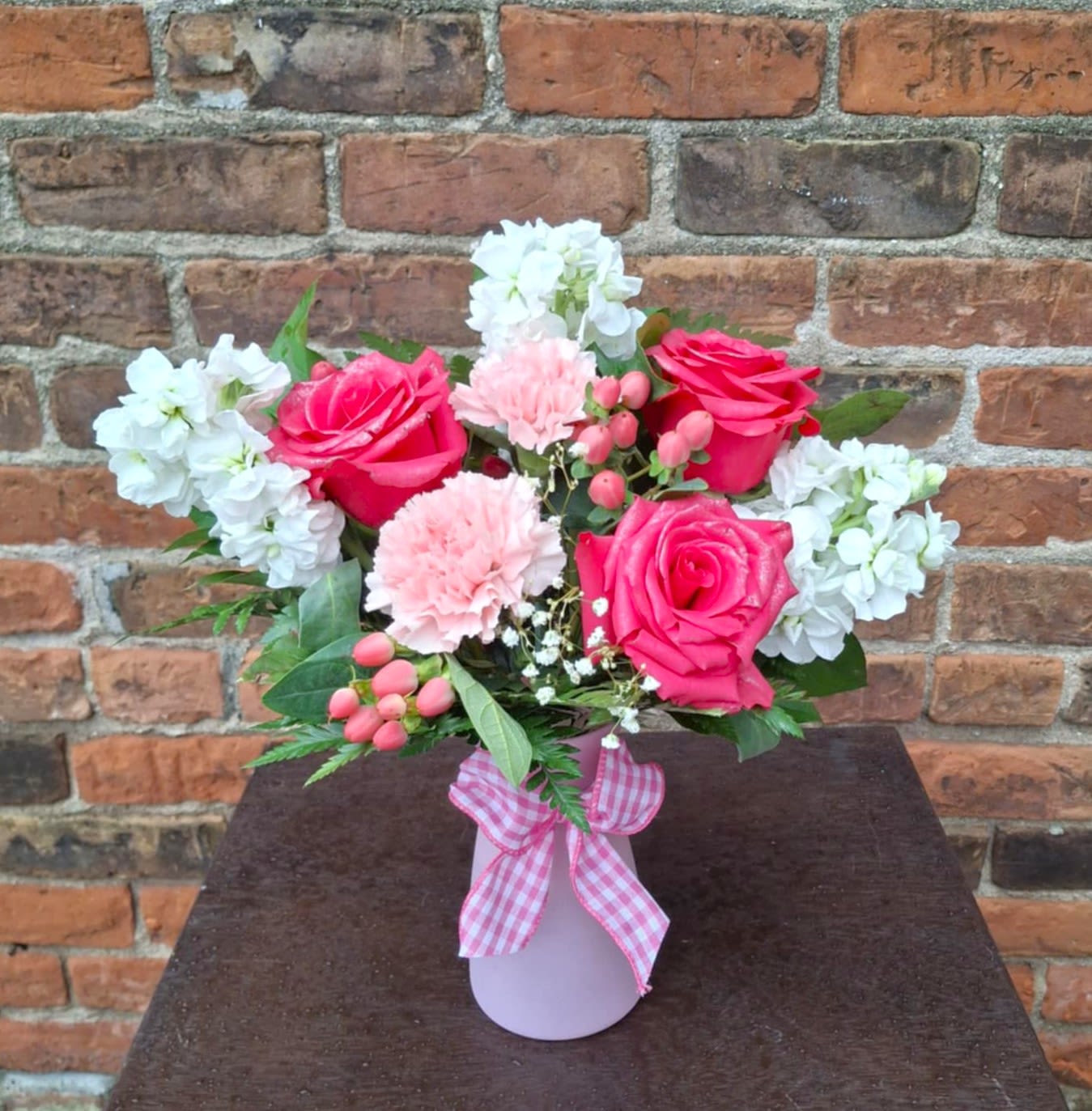 Pink roses and carnations in a vase with white flowers and a gingham ribbon