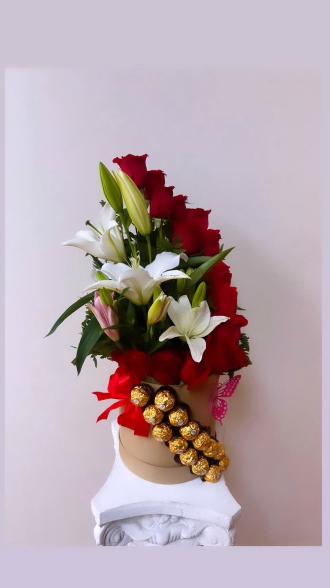 Red and white lily arrangement with gold chocolates on a hat box