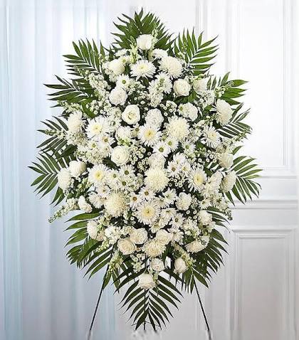 Eternal Grace Standing Spray - An elegant all-white standing spray designed to honor with grace and timeless beauty. Featuring a lush composition of premium white blooms such as roses, carnations, chrysanthemums, and filler flowers, accented with fresh seasonal greenery, this tribute creates a serene and sophisticated display. Arranged on a standing easel, the design symbolizes peace, remembrance, purity, and everlasting love — making it a meaningful expression of sympathy and support.
