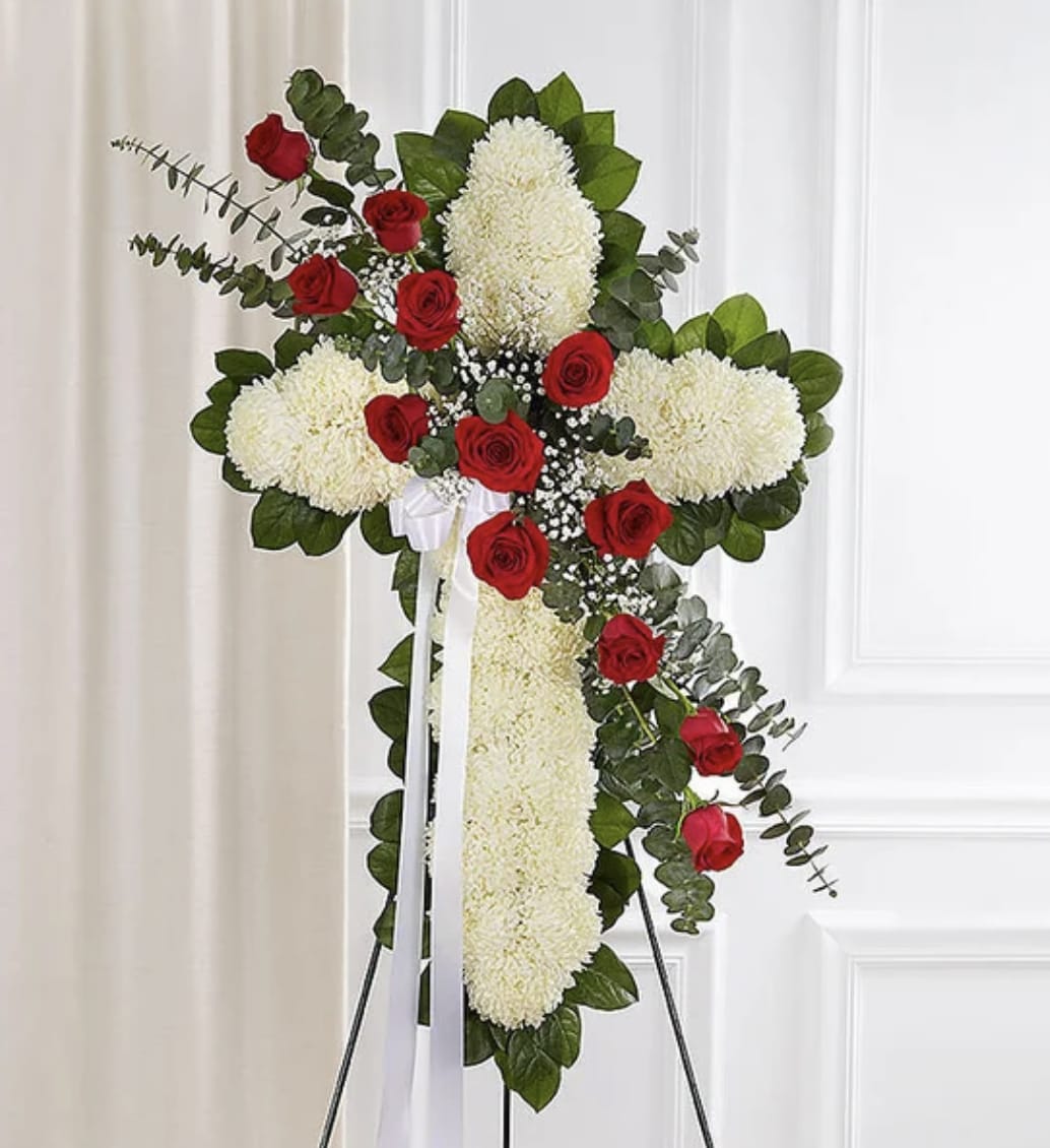 Eternal Faith Tribute - A timeless all-white floral cross designed with elegance and reverence, accented by a striking cascade of red roses flowing gracefully across the design. Crafted with premium white chrysanthemums and carnations, this standing tribute symbolizes peace, faith, and eternal rest, while the rich red roses and mini-carnations represent deep love, honor, and devotion. Displayed on a standing easel, this meaningful arrangement offers a beautiful expression of sympathy and remembrance.
