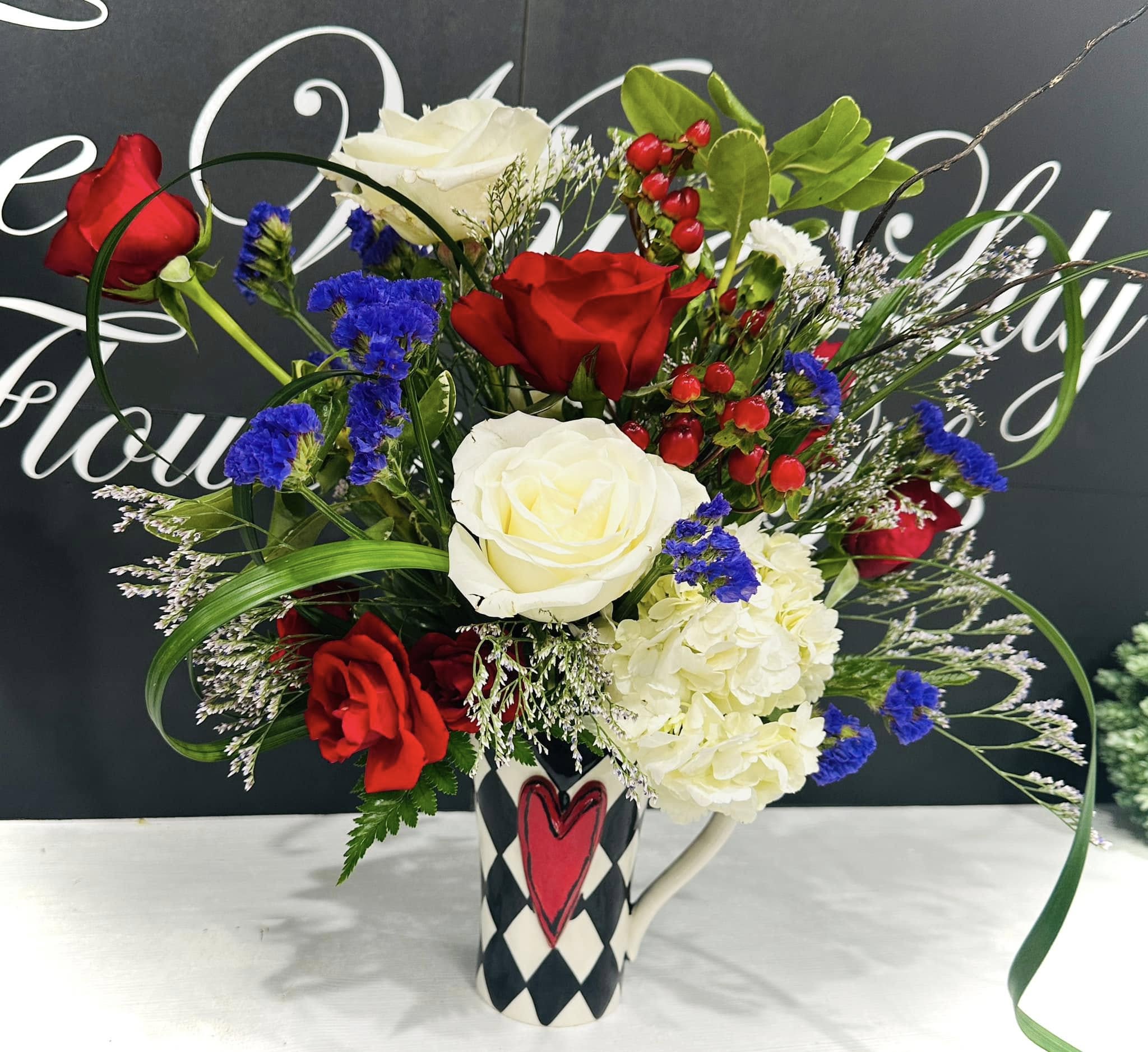 Bouquet of red and white roses with blue filler flowers in a patterned mug