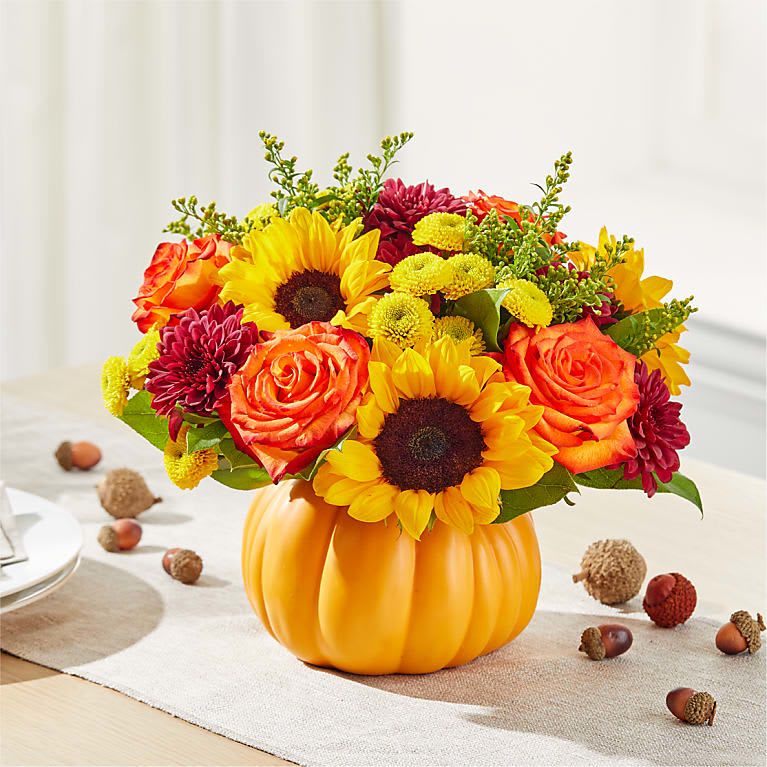Mixed bouquet in a pumpkin-shaped vase with sunflowers, roses, and mums