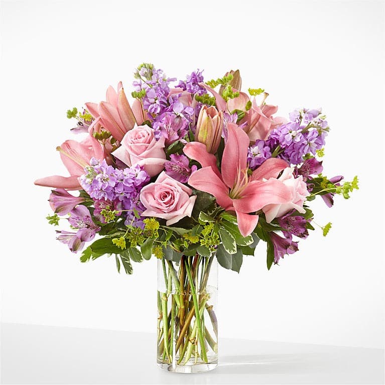 Pink lilies, roses, and purple flowers in a clear glass vase