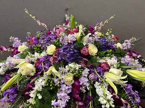 Large low spray of purple, lavender, and white roses, lilies, hydrangeas, and orchids in a dense arrangement