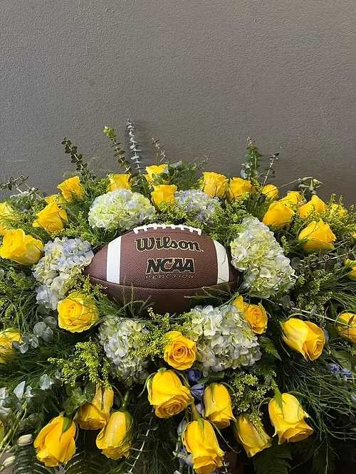Yellow roses and pale hydrangeas arranged around a football centerpiece