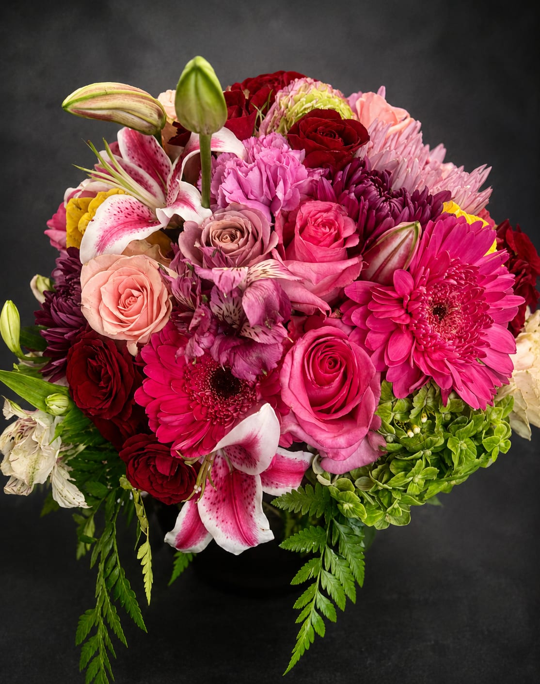Bright and Happy - A lush, rounded bouquet bursting with pinks, reds, lavender and white, Bright and Happy is a flower arrangement that reads like a joyful celebration. Perfect as a birthday bouquet, anniversary arrangement, or a "just because" surprise, the prominent pink gerbera daisies and roses give the design an immediate, smiling focal point while spotted lilies and unopened lily buds add height and graceful texture.  This dense, full arrangement mixes hydrangea-like blooms, alstroemeria, chrysanthemums and stock for layered texture and a generous, garden-fresh look. Fresh green accents and a few pale blooms soften the saturated pinks and magentas, while pops of orange and yellow warm the palette. Arranged in a simple vase, it's compact enough for a bedside table or desk yet full enough to make a statement in an entryway or dining table.  Send Bright and Happy to celebrate graduations, new babies, retirements, housewarmings, or to lift someone's spirits when they're under the weather-she'll feel truly seen and cared for. Available in a standard vase size; stems arrive ready to display with simple care: keep fresh water, trim stems every few days, and place away from direct heat to extend vase life.