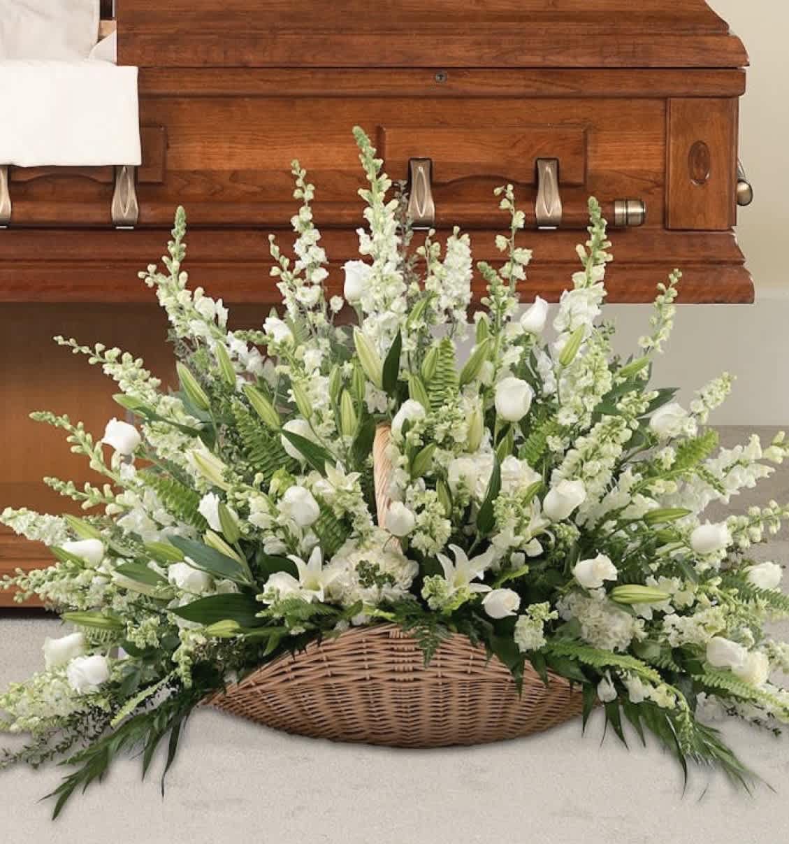 White floral spray in a wicker basket in front of a wooden casket