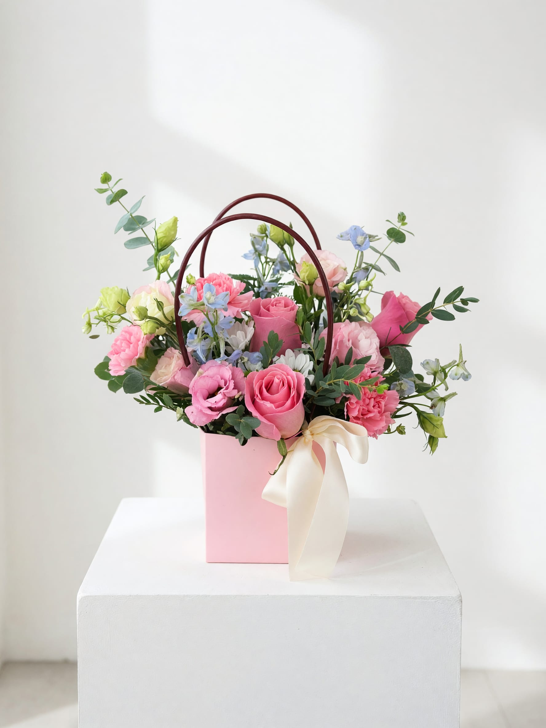 Pink and blue mixed flower arrangement in a pink gift box with ribbon handles