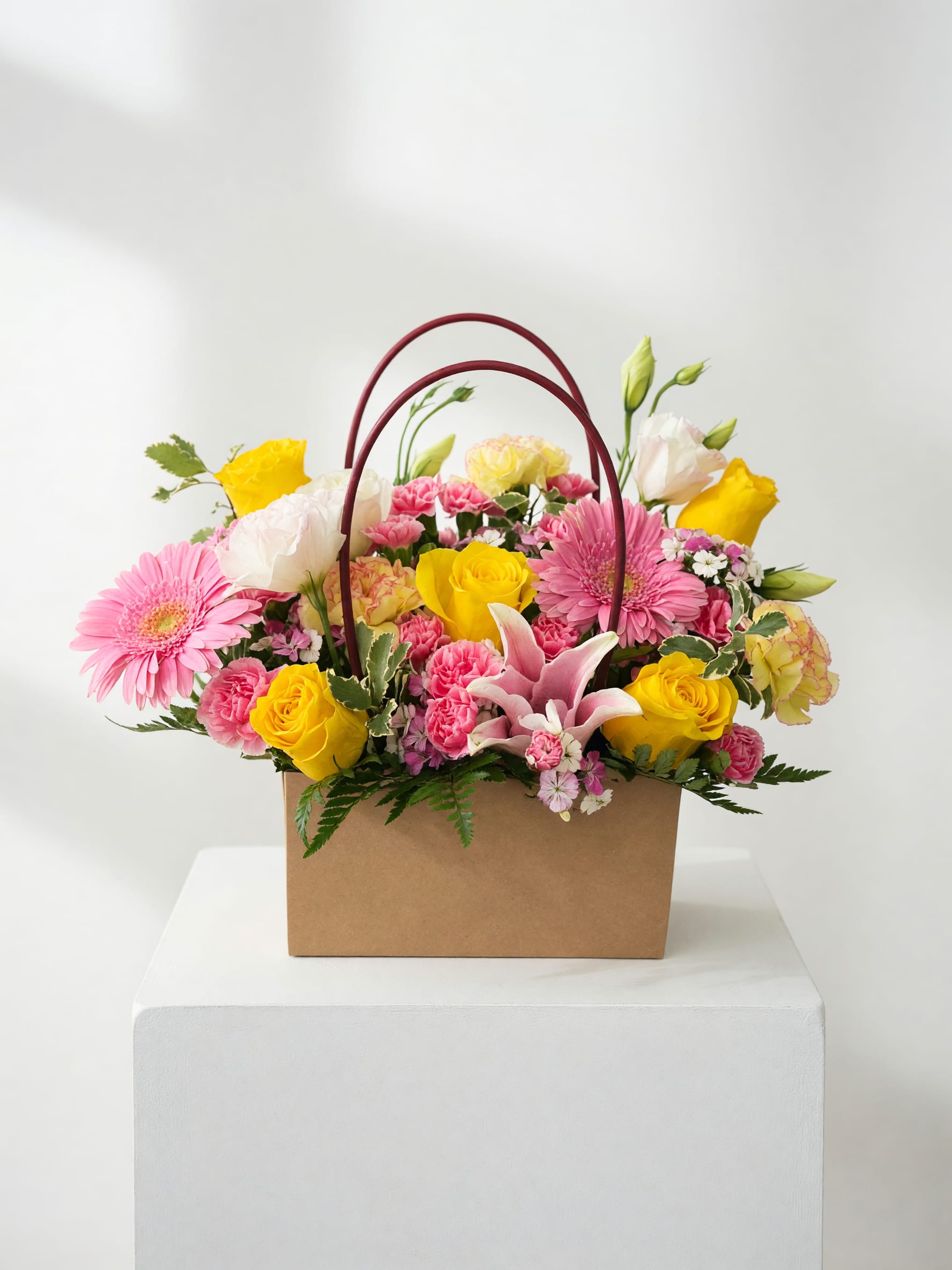 Mixed pink and yellow flowers arranged in a brown handled box