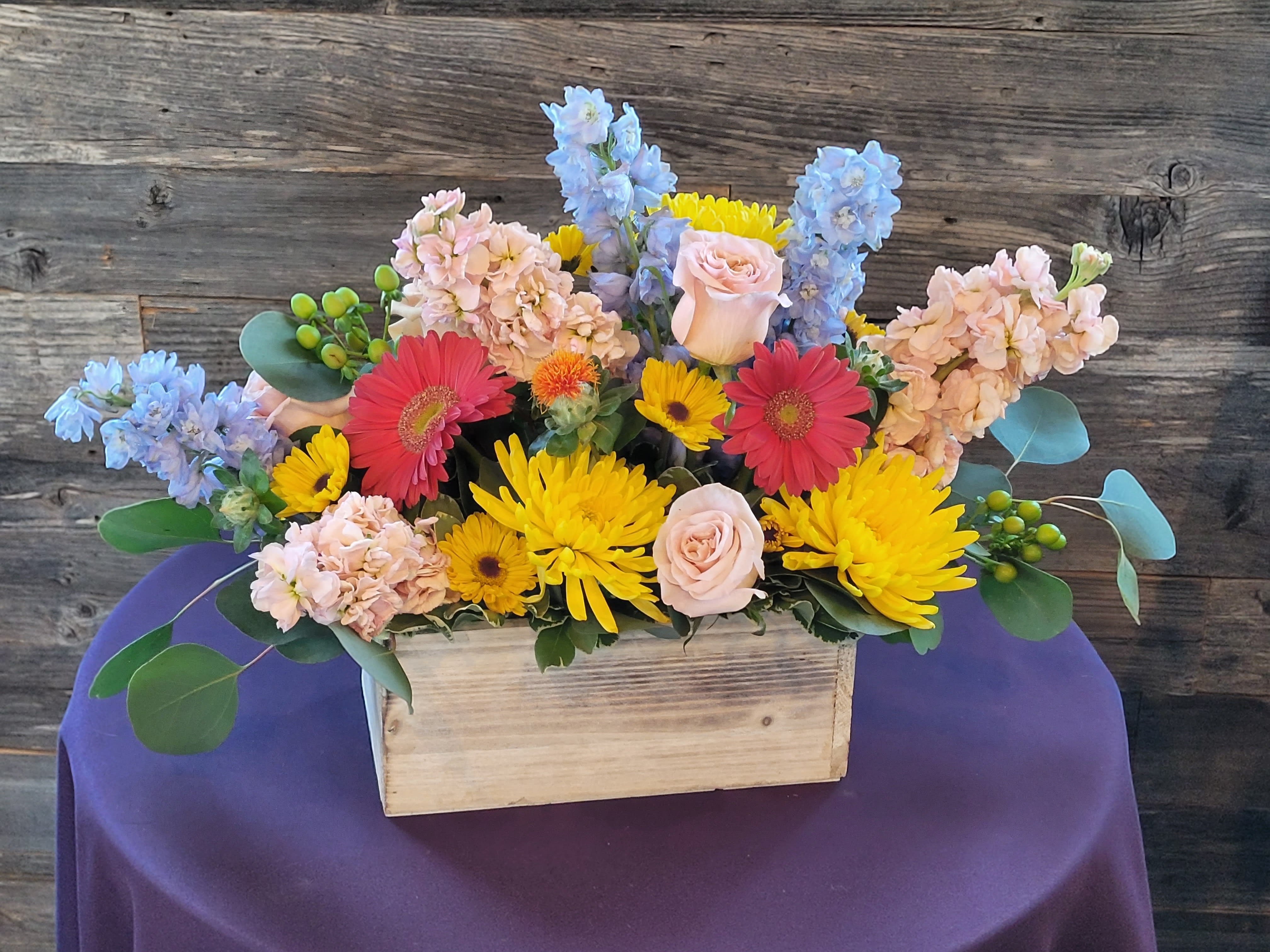 Mixed bouquet in a wooden box with pink, yellow, blue, and red flowers