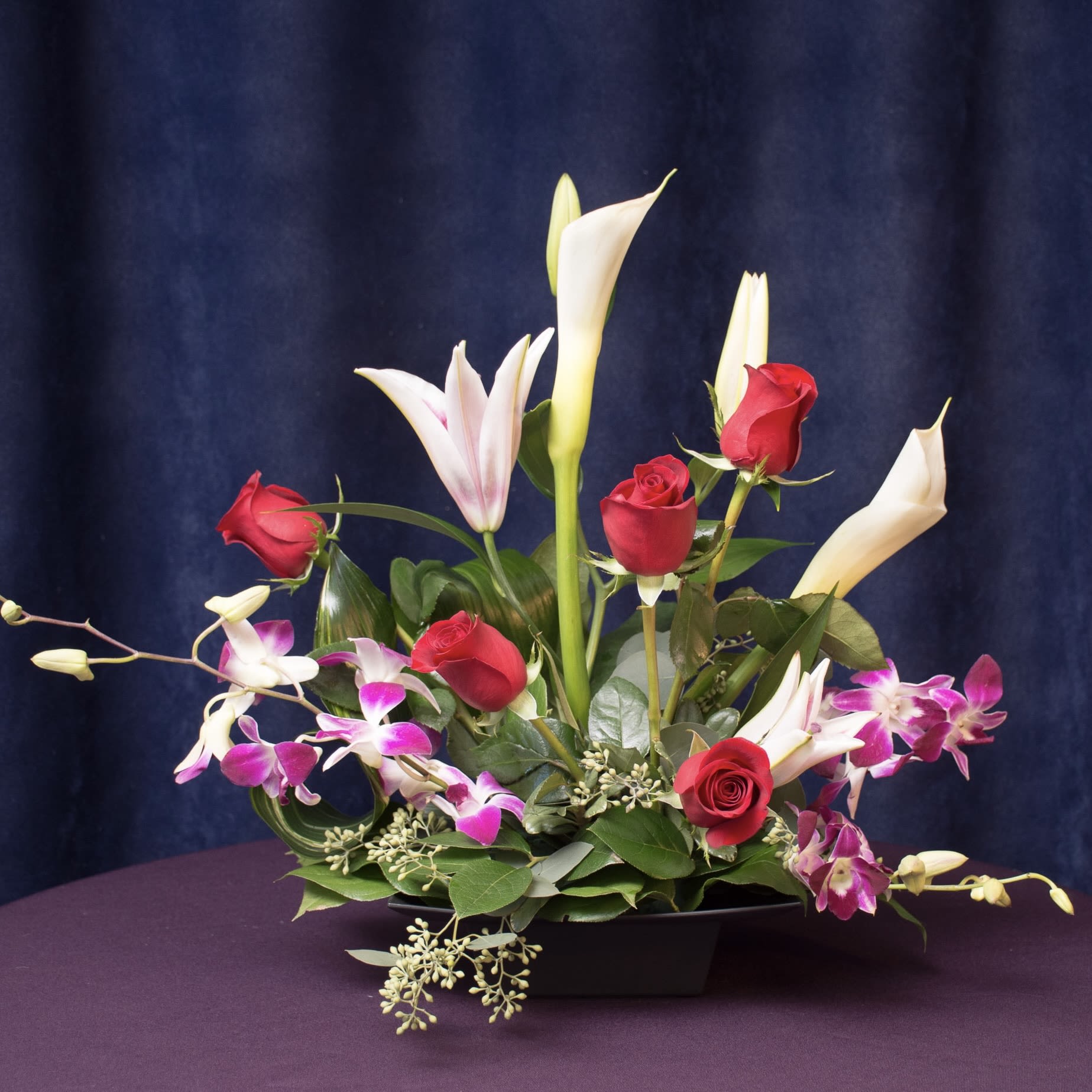 Arrangement of red roses, white calla lilies, and pink orchids in a black vase