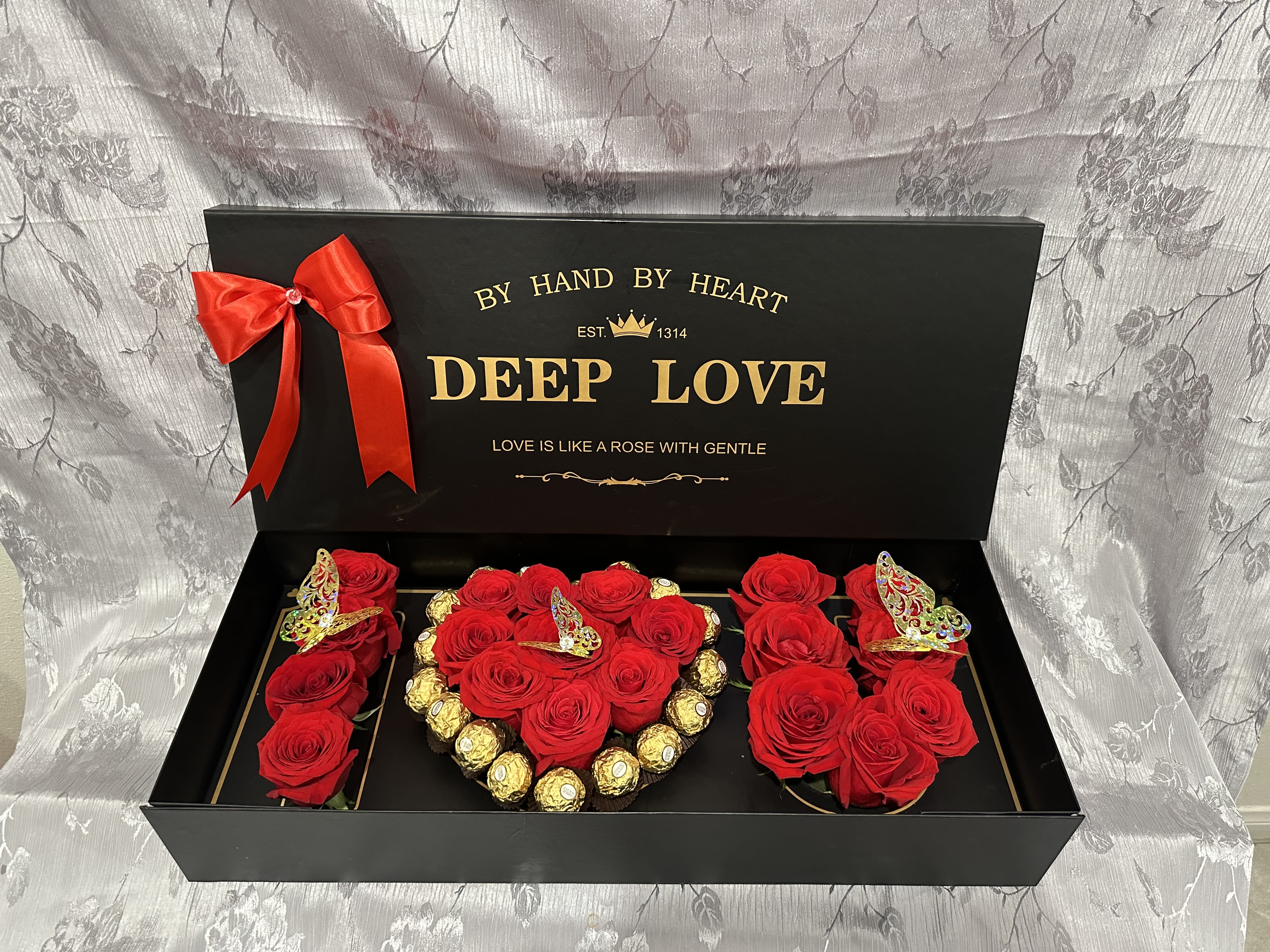 Black gift box with red roses, gold chocolates, and a red ribbon