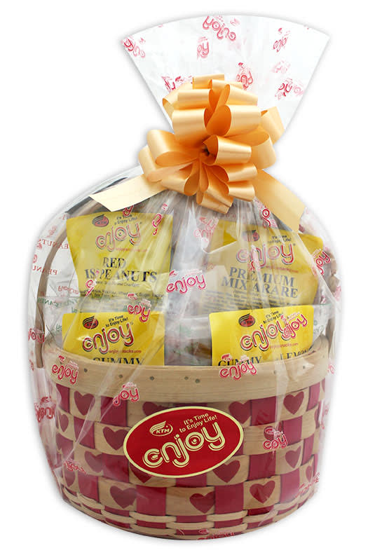 Wrapped snack gift basket with yellow packages in a heart-patterned woven basket and large peach bow