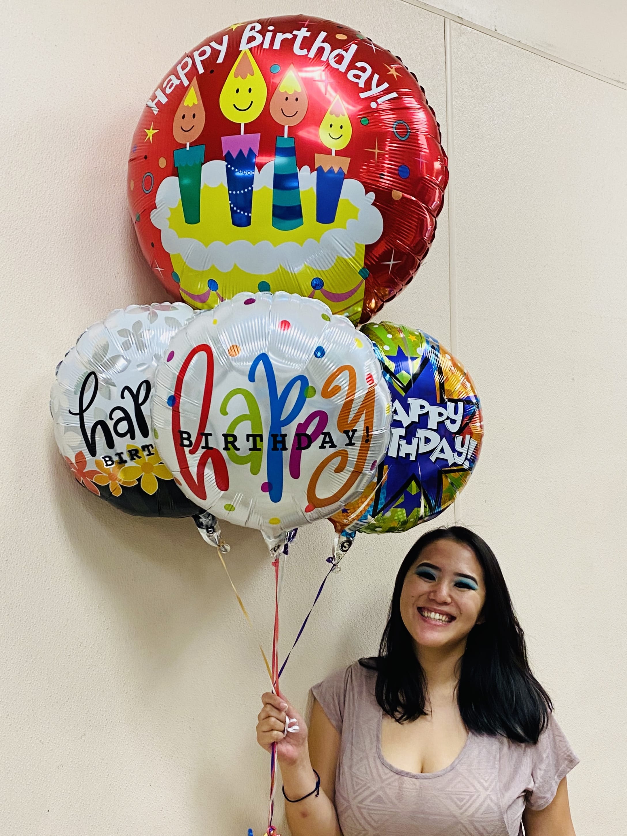 Smiling woman holding a cluster of colorful round Happy Birthday balloons.