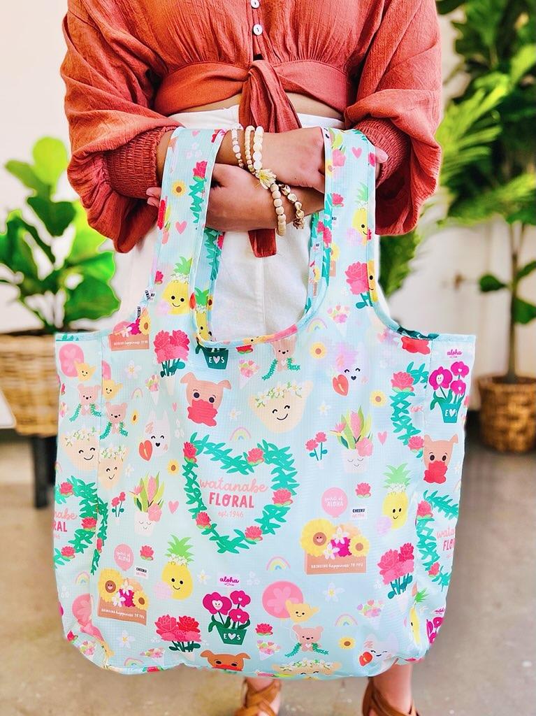 Pastel blue reusable tote bag with colorful cartoon flowers and characters held in front of a person.