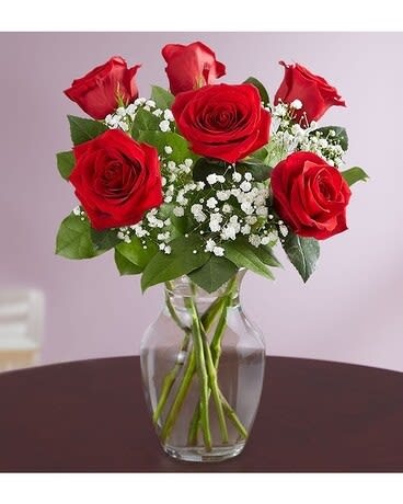 Red roses arranged in a clear glass vase with white filler flowers