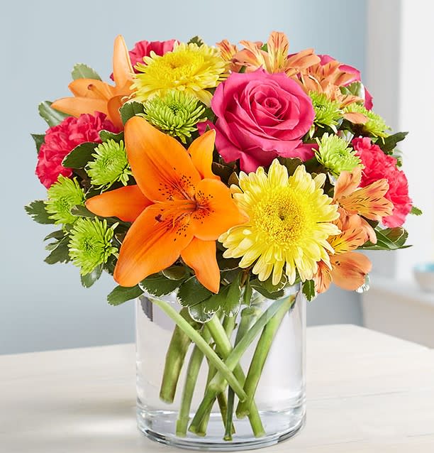 Mixed bouquet of roses, lilies, and chrysanthemums in a clear glass vase