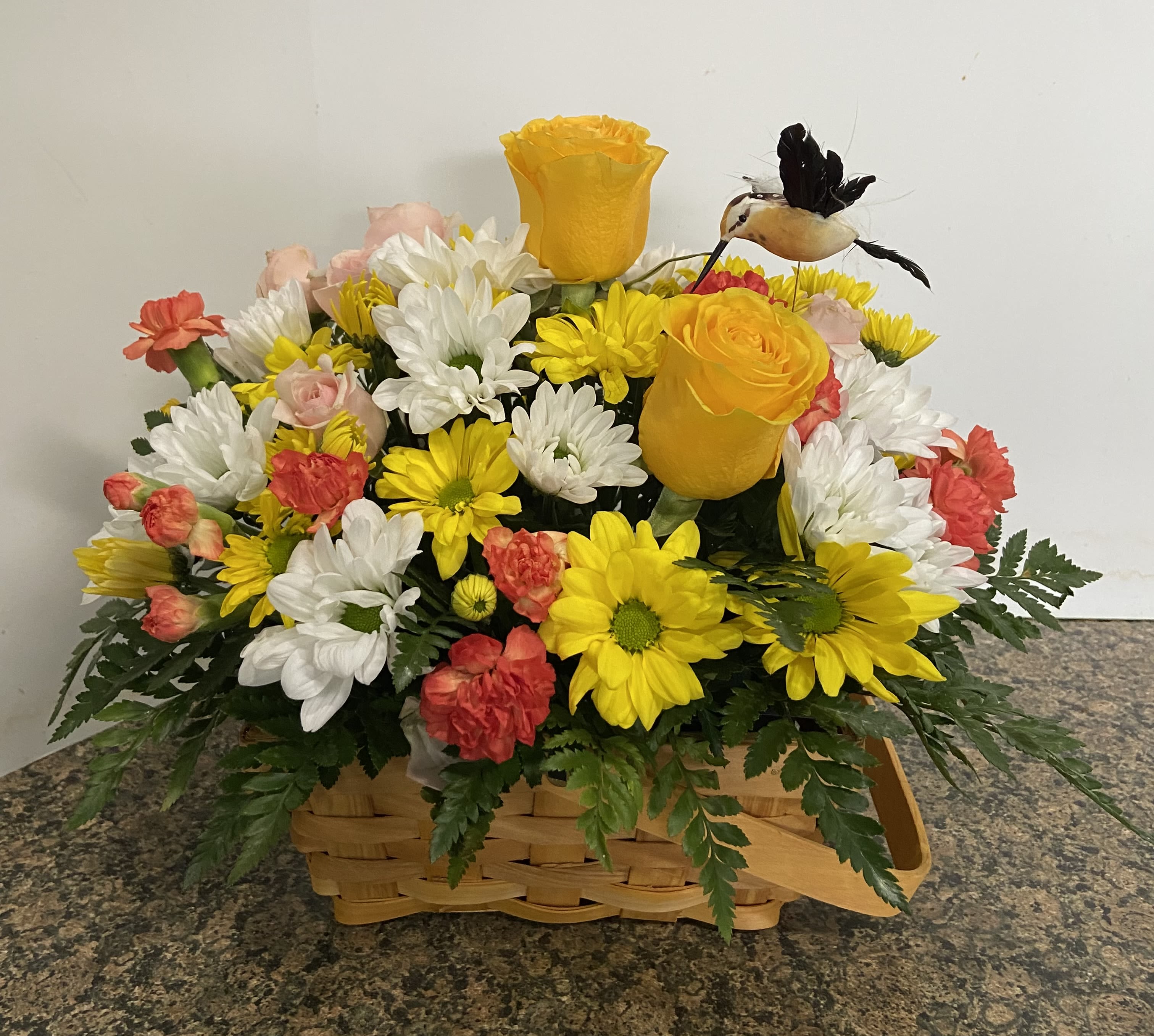 Basket arrangement of yellow and white daisies with pink roses and a small bird ornament