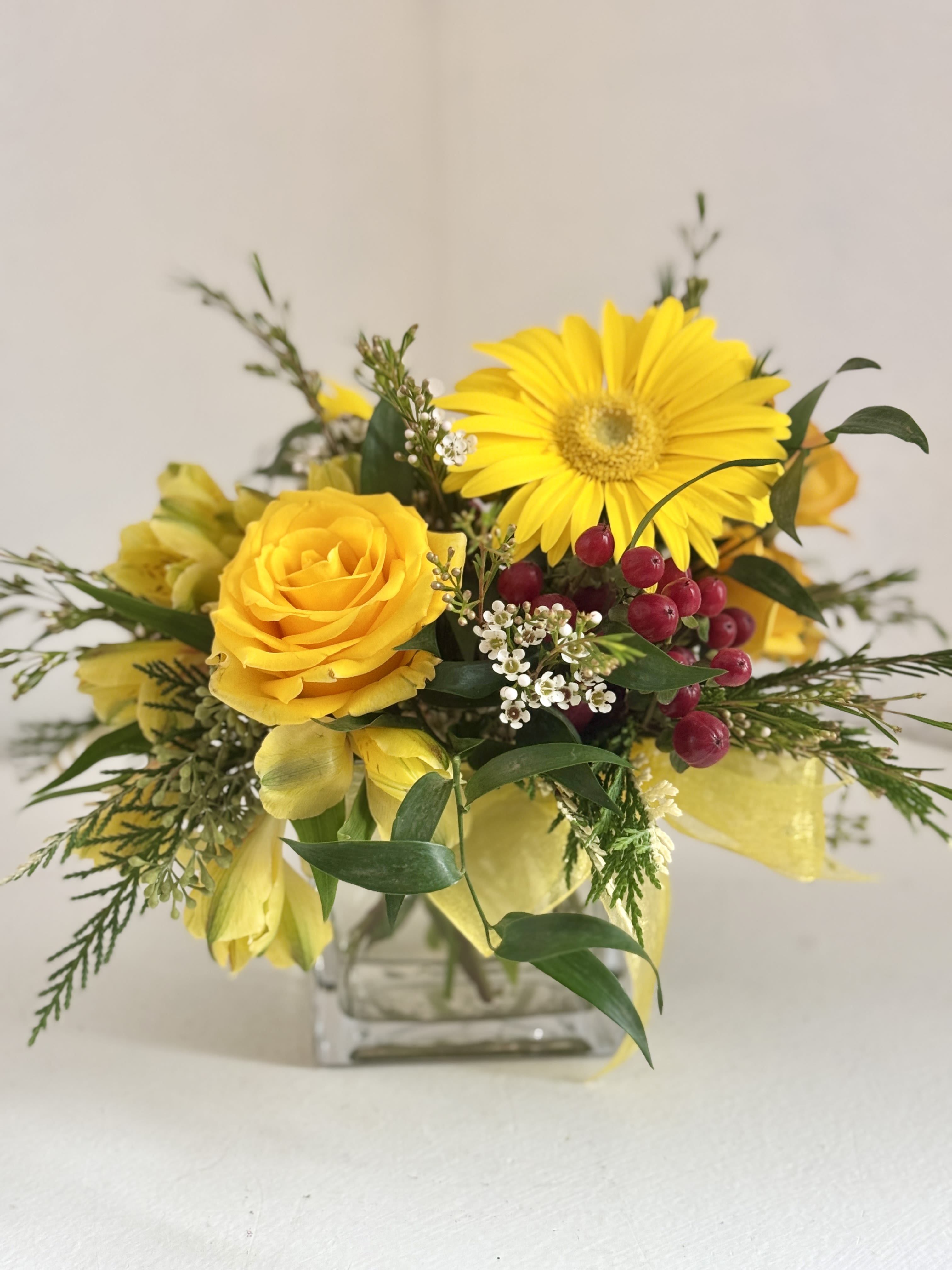 Yellow roses and a gerbera daisy in a glass vase with red berries