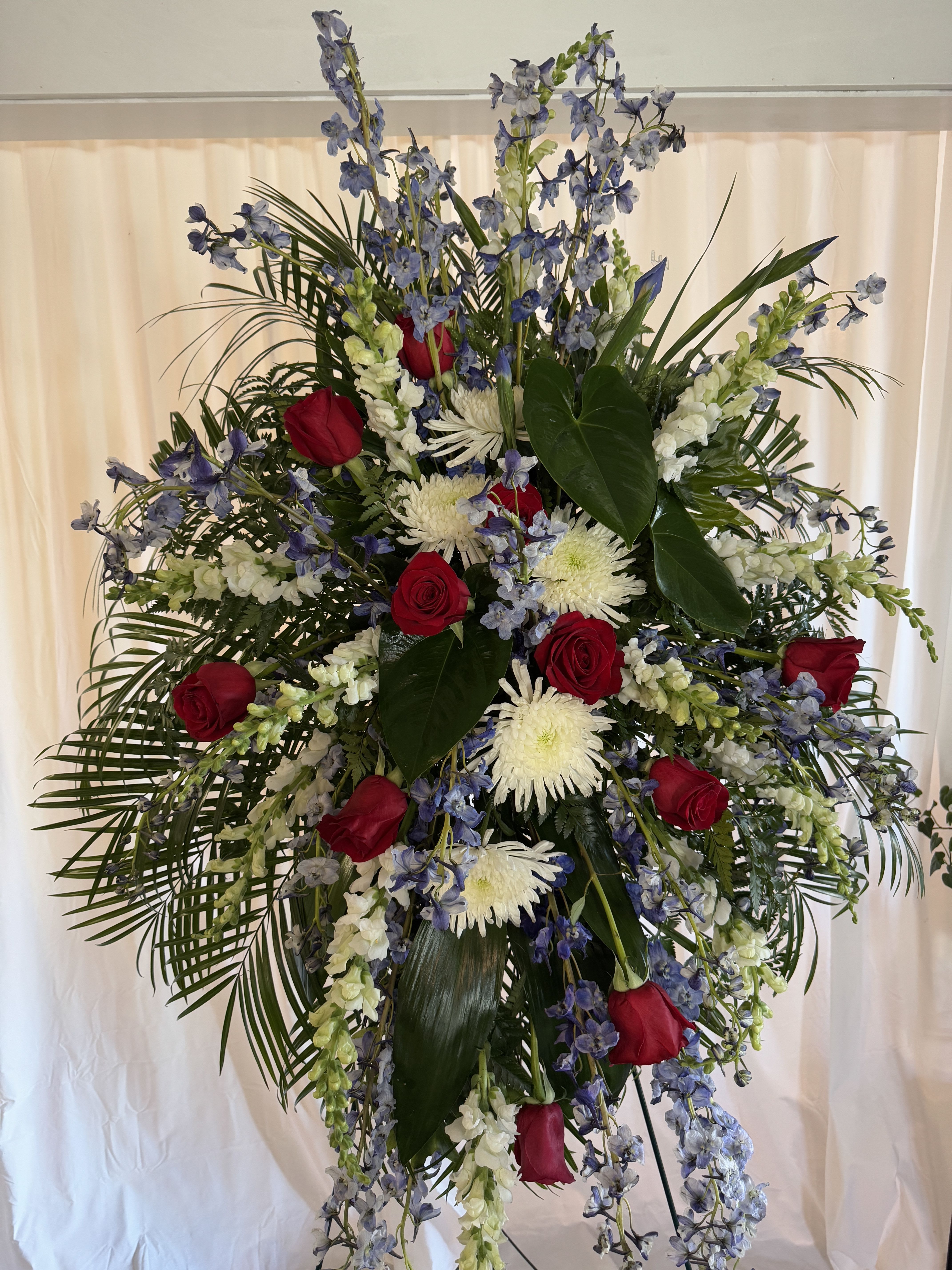 Tall standing floral spray with red roses, white blooms, and blue flowers