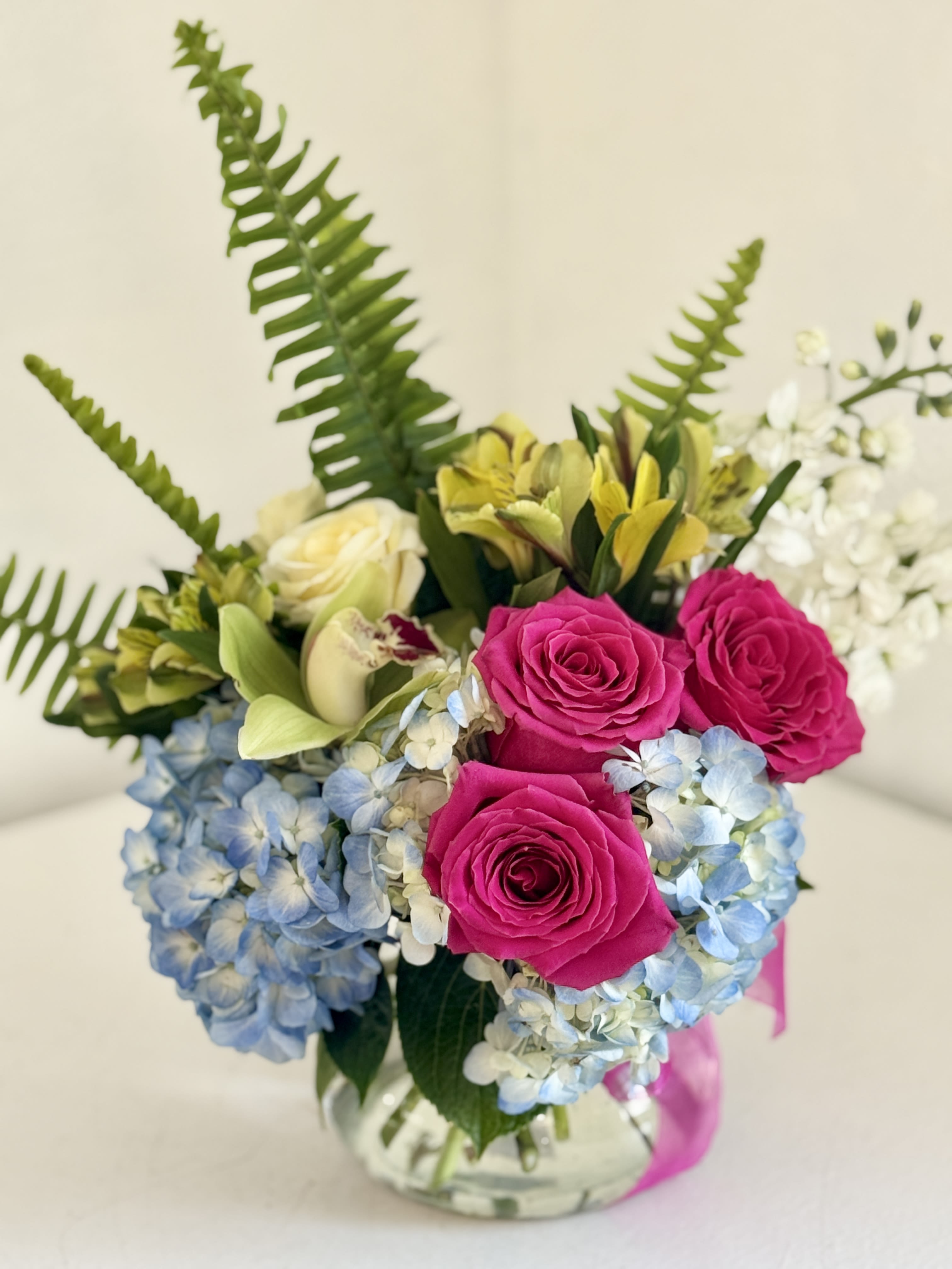 Bouquet of pink roses, blue hydrangeas, and yellow lilies in a glass vase